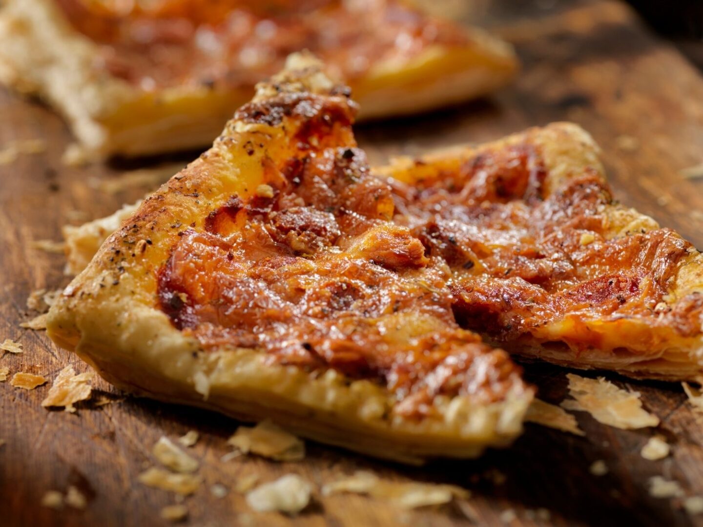 Cheese and tomato puff pastry piece slice on a wooden serving board.