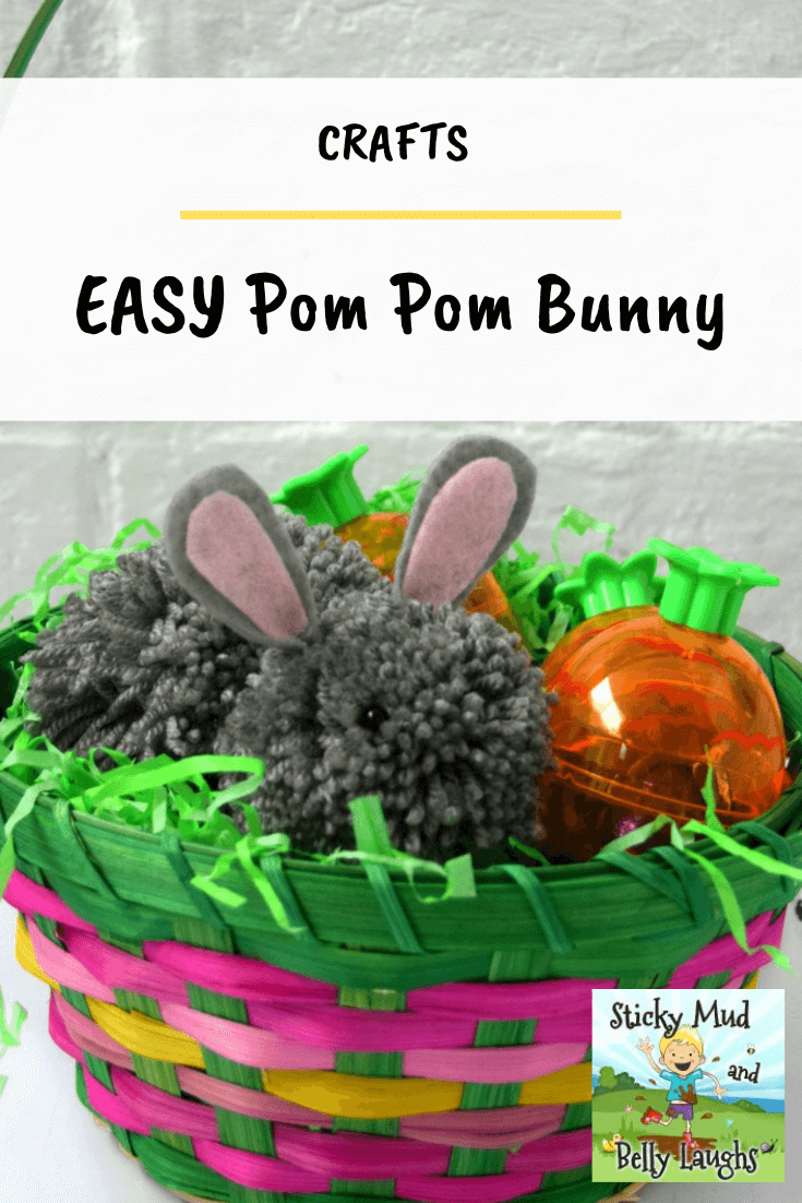 A grey pop pom bunny in a multicoloured basket and green shredded tissue paper.