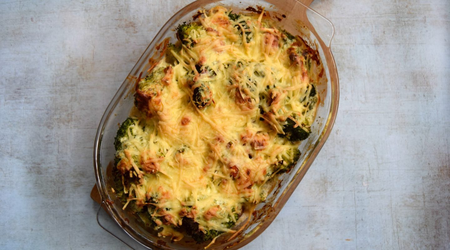 A tasty cheesy recipe in a glass oven dish resting on a wooden serving platter.
