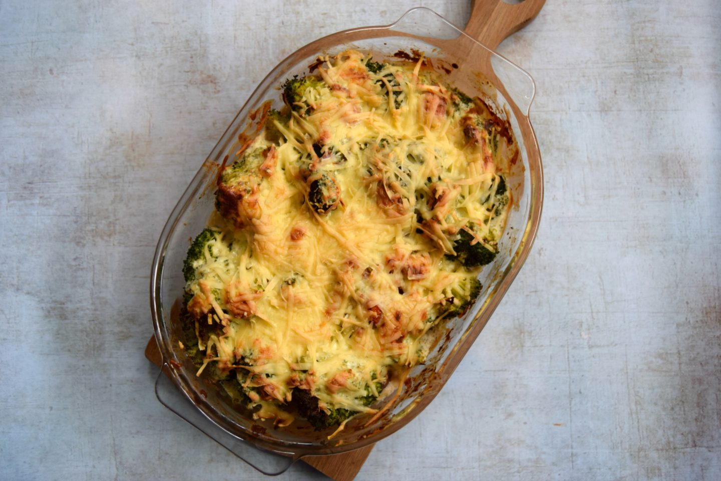 A tasty cheesy recipe in a glass oven dish resting on a wooden serving platter.