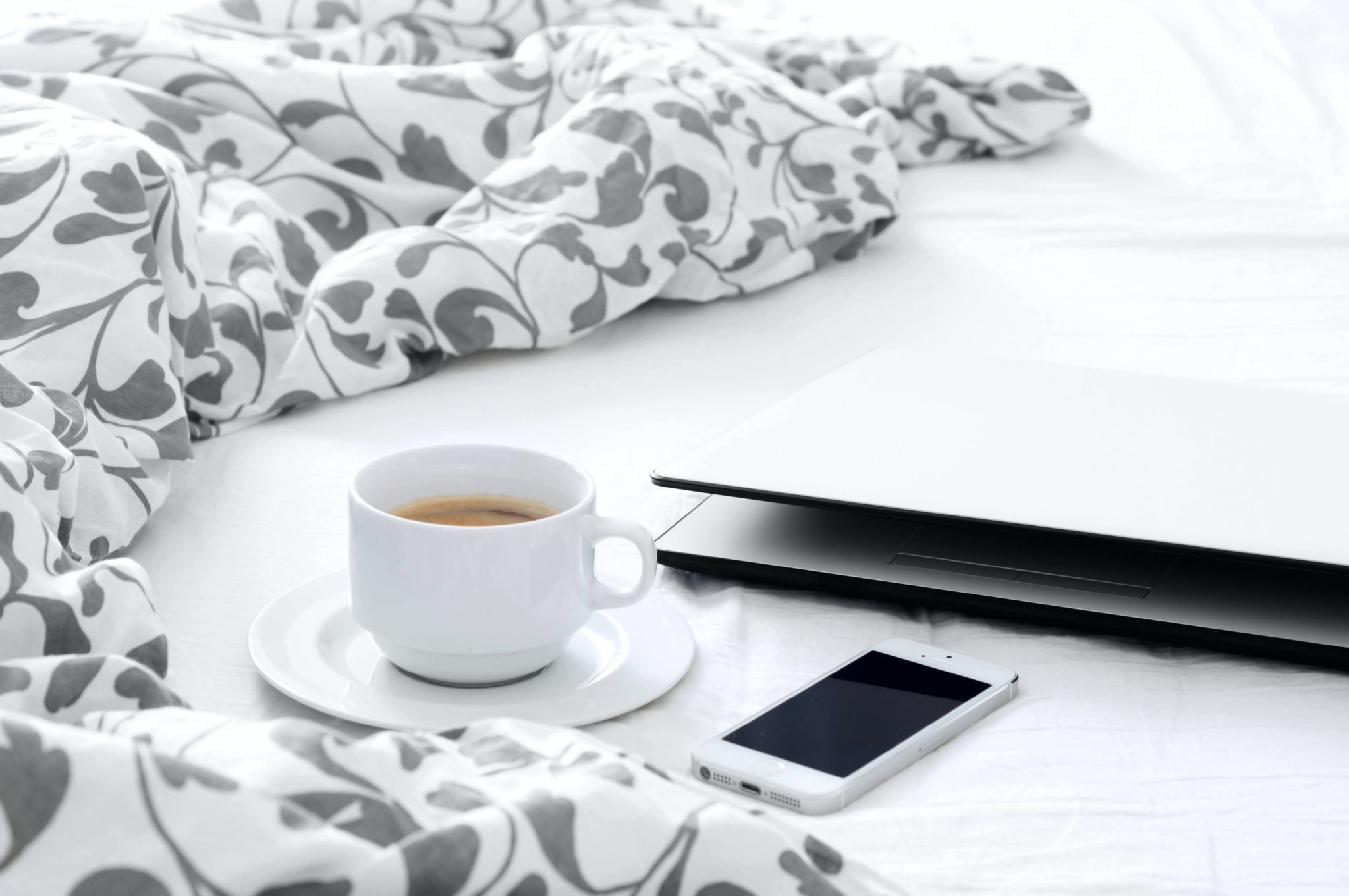 Working from home. A laptop, a phone and a cup of tea next to a duvet.