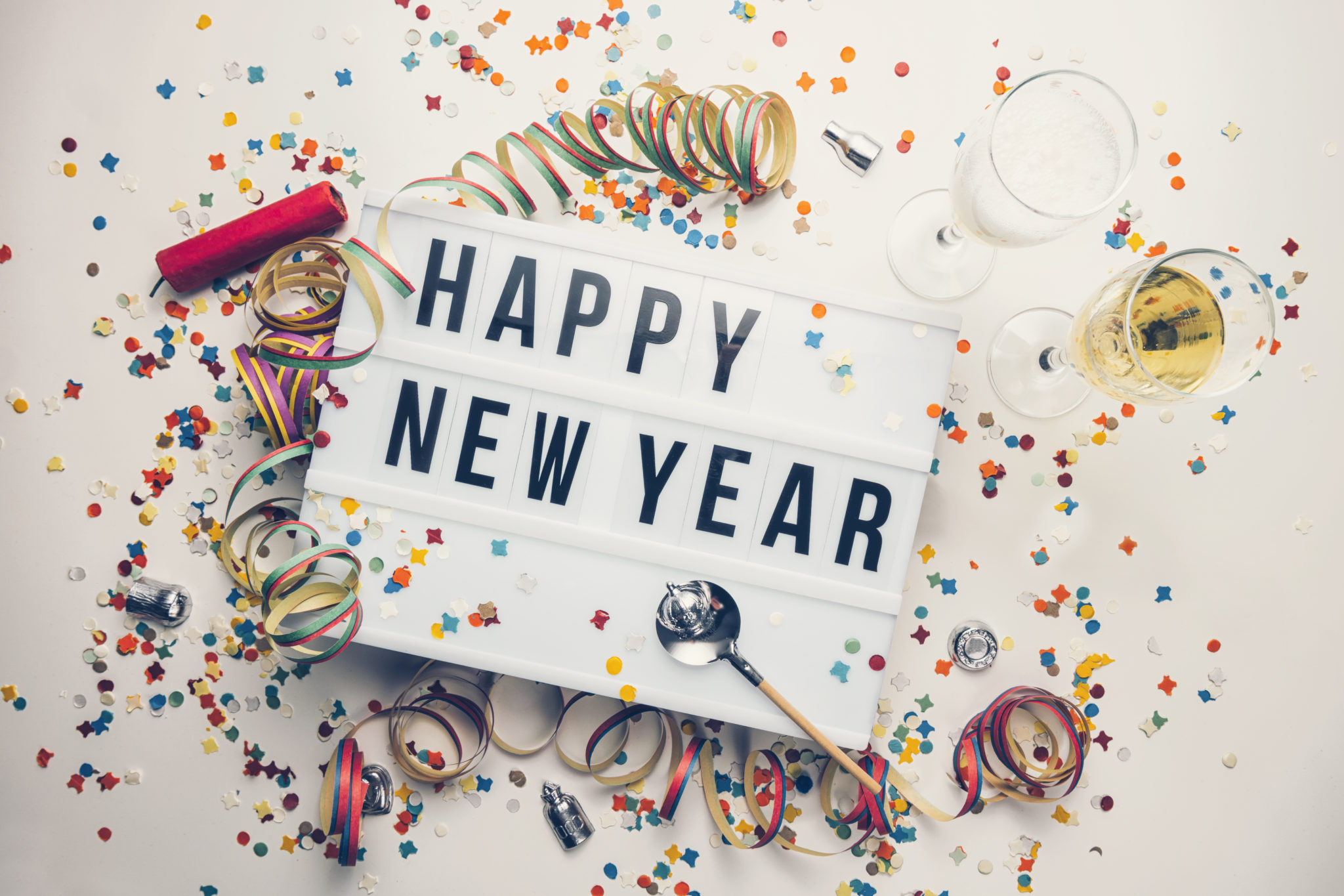 Happy New Year sign with confetti and glasses of champagne.