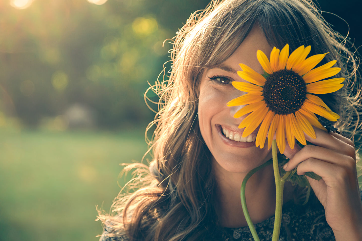 A lady smiling and holding up a sunflower.