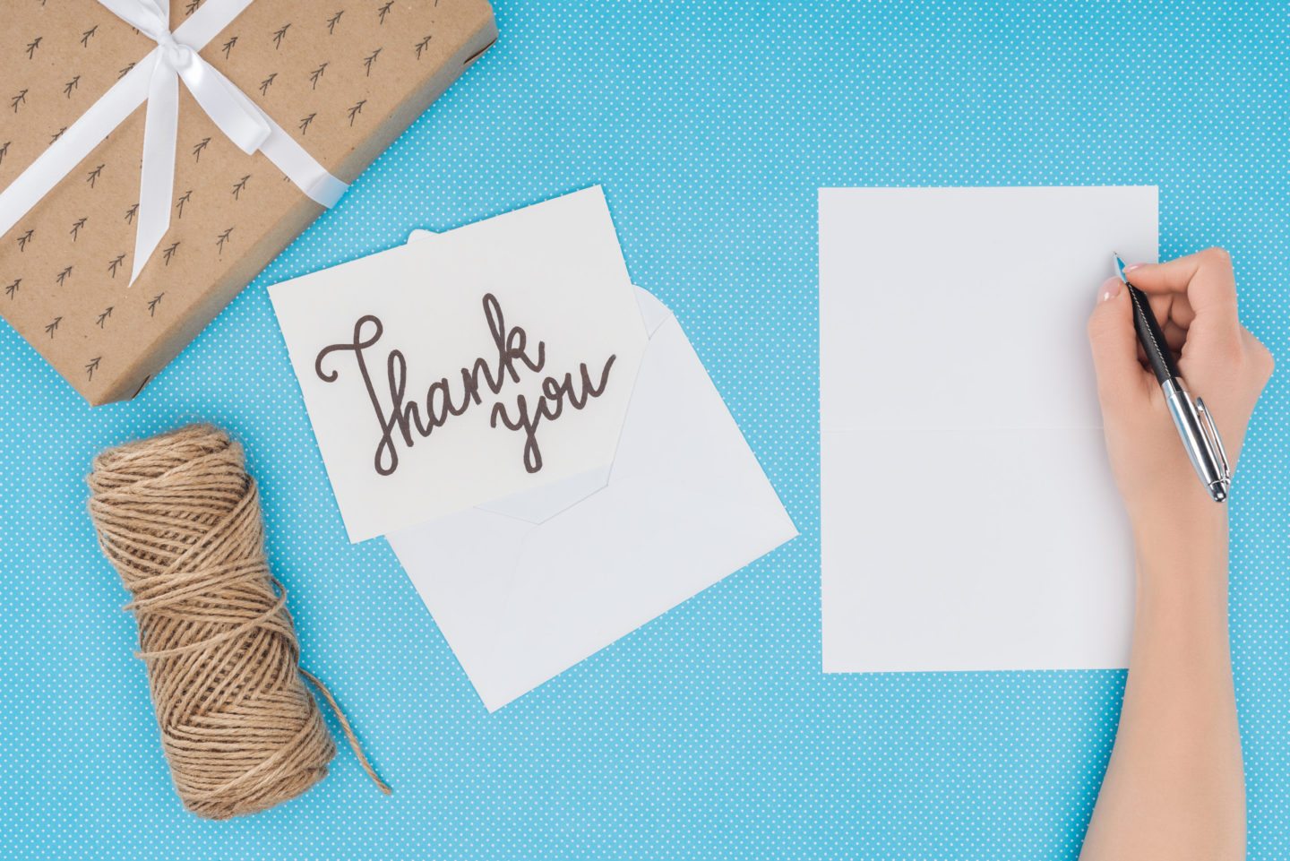 Somebody writing a thank you card on a desk top with a parcel and twine.