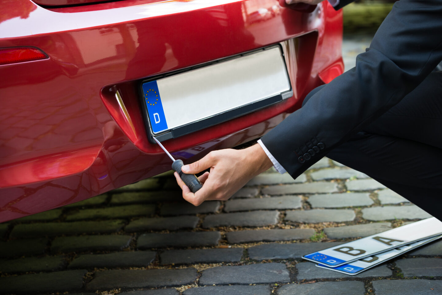 A car registration plate. A man replacing a number plate on a red car