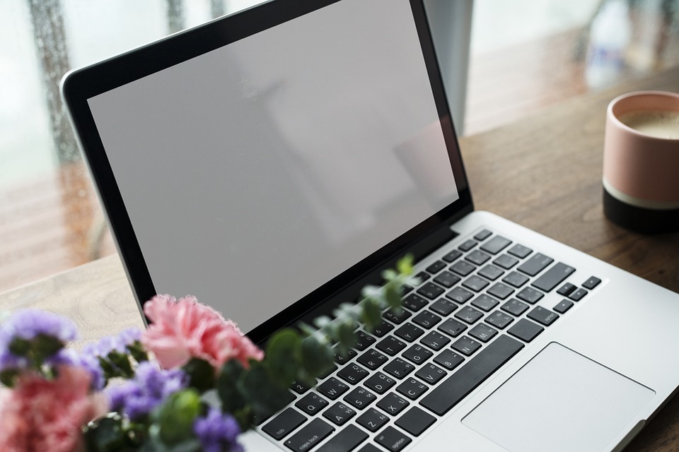 A desk with an open laptop, pink and purple flowers and a mug of tea.