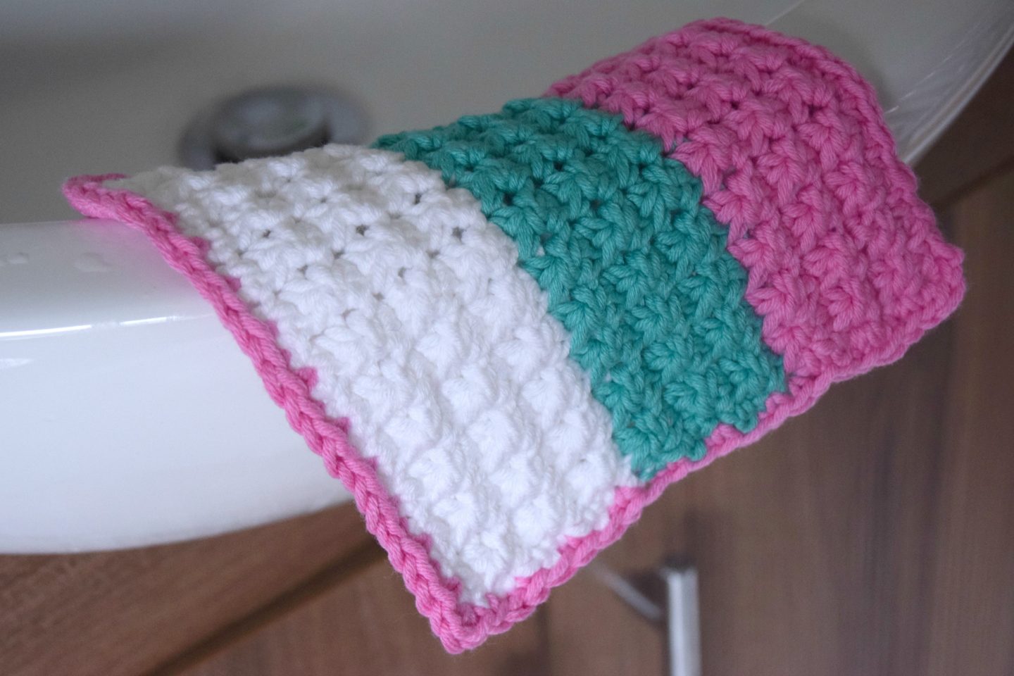 Crochet pastel wash cloth in pink teal and white cotton blend yarn.