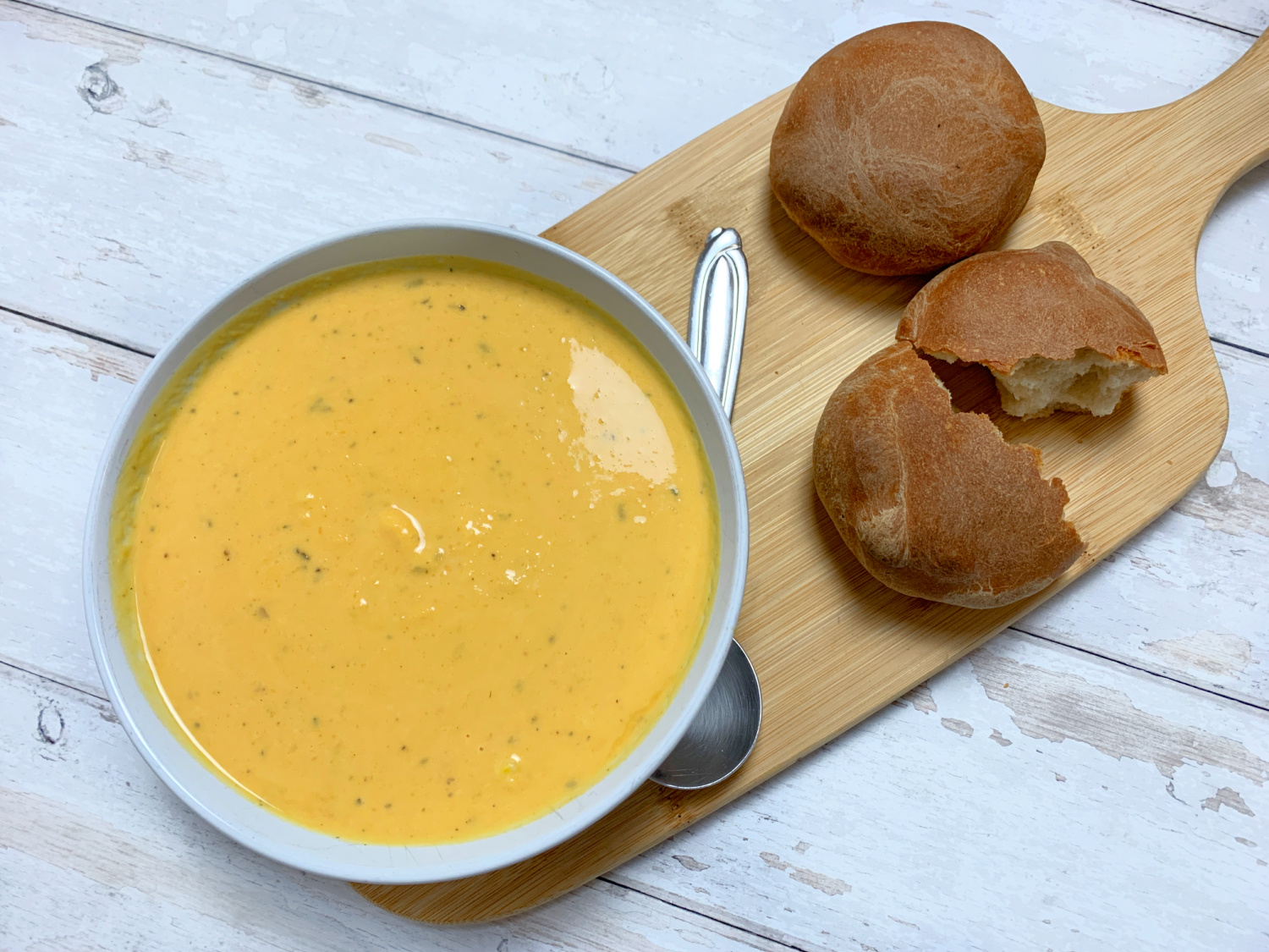A bowl of butternut squash soup with homemade bread rolls. Served on a wooden board.