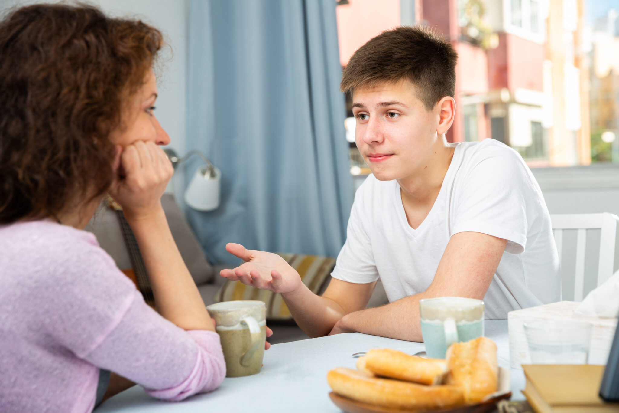 A mother and son having a discussion at the table with a cup of tea each.