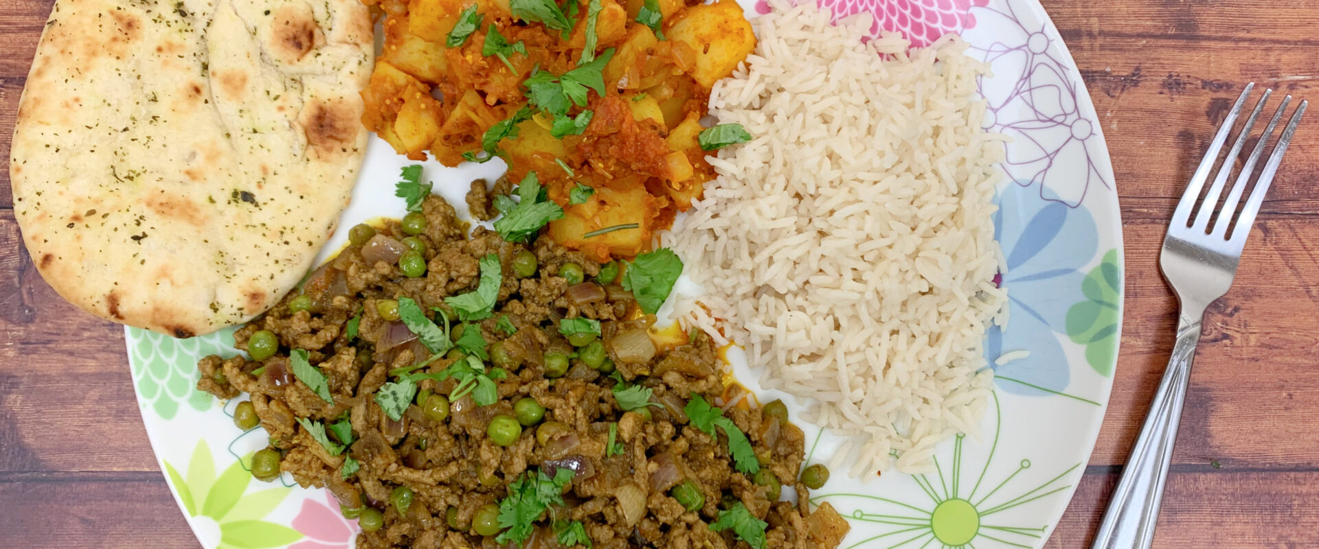 A plate of keema curry, basmati rice, bombay potatoes as a side and a mini naan bread.