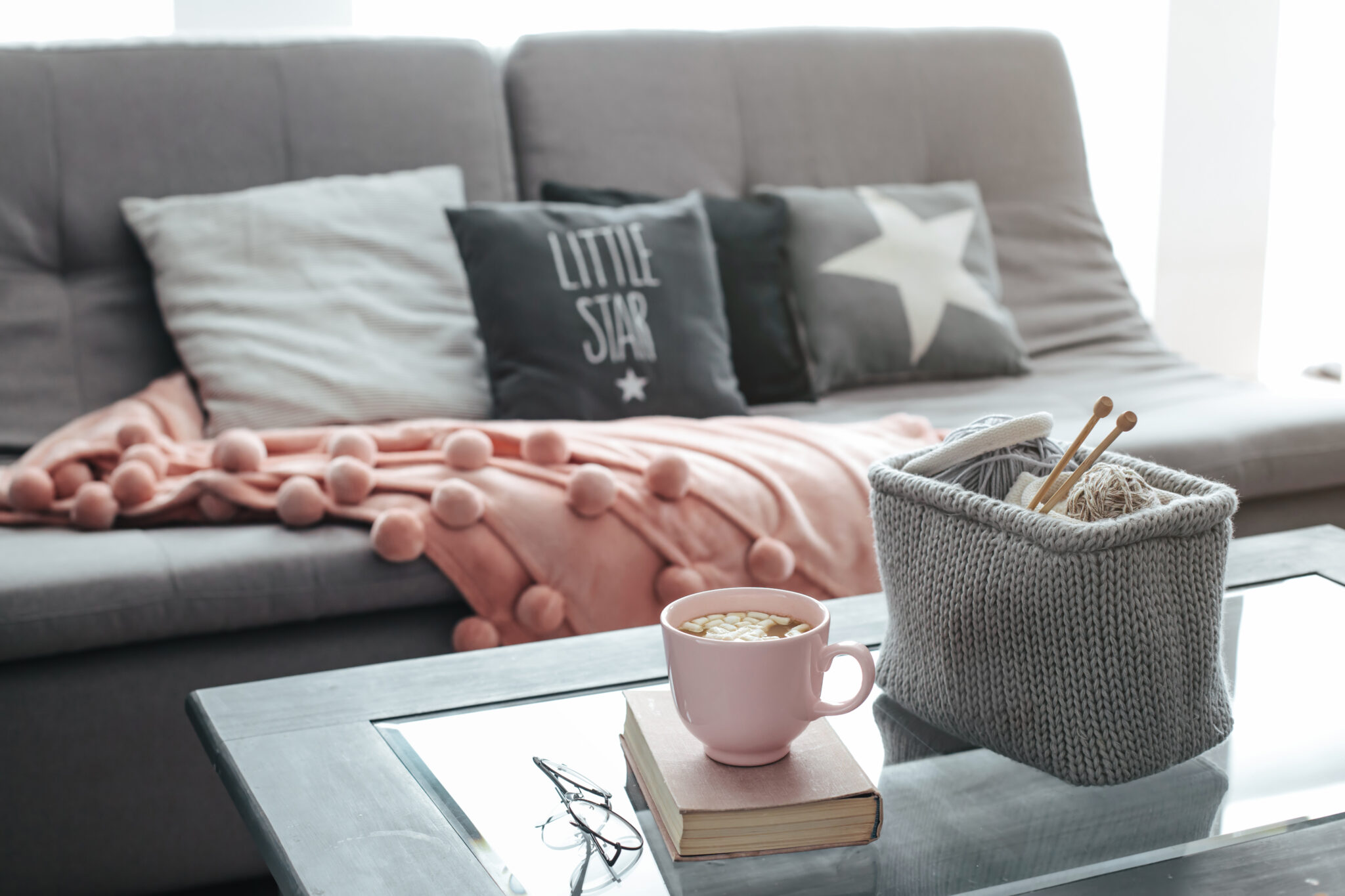 a cosy living room with a grey sofa and a cosy throw draped over it. There is also a hot chocolate and crochet needles on a coffee table.