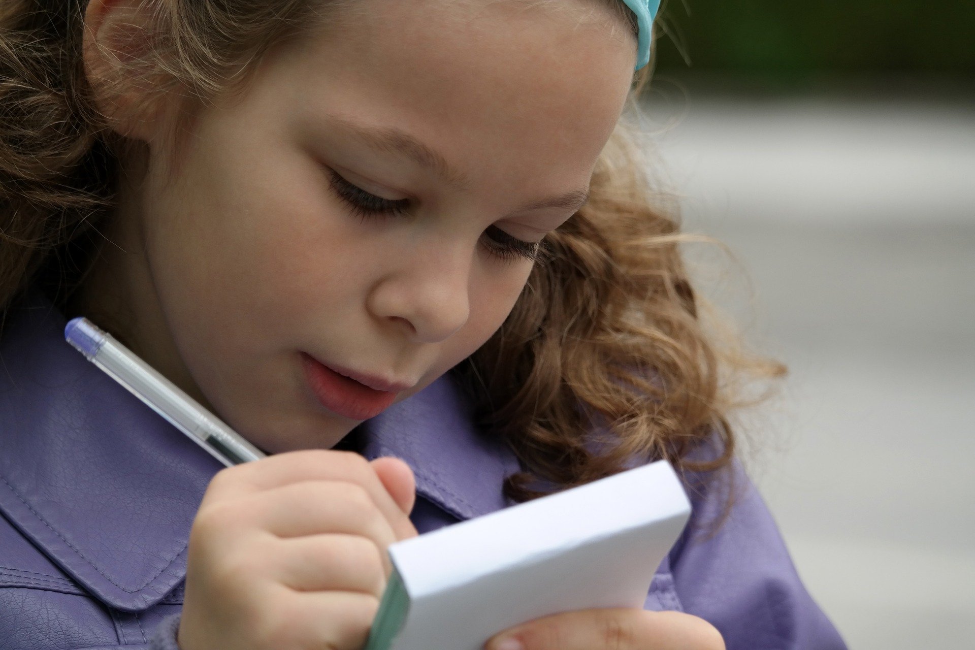 A young girl wearing a purple coat writing on a notebook