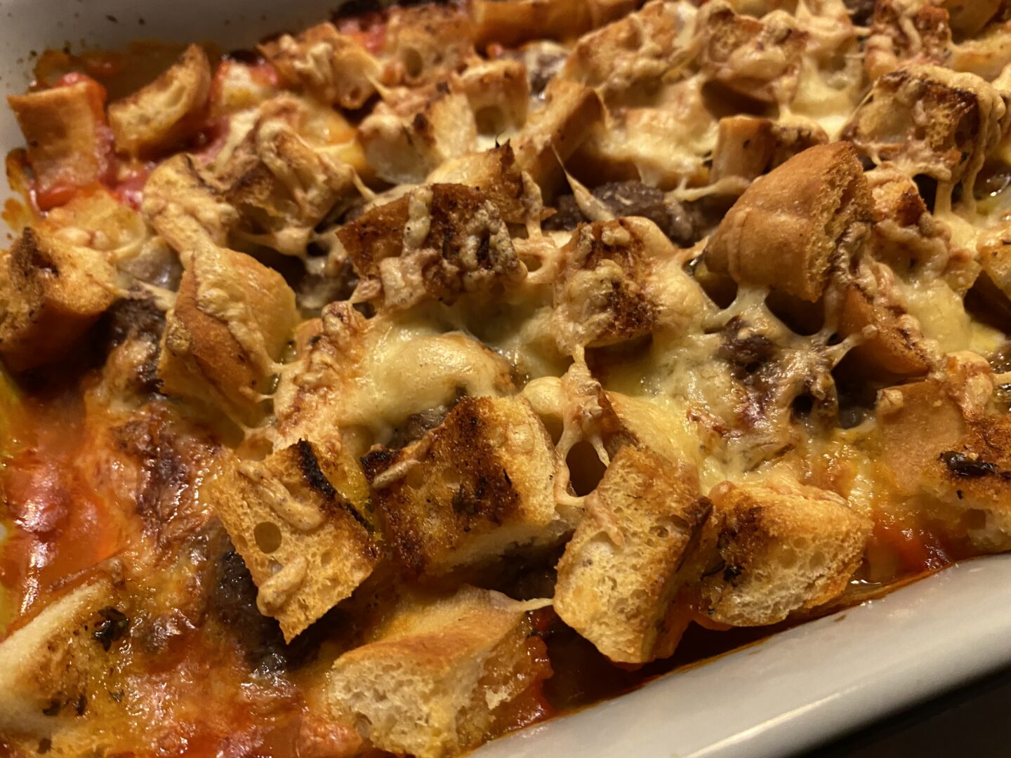 A close up of meatballs, chunks of crispy garlic bread topped with cheese in an oven tray.