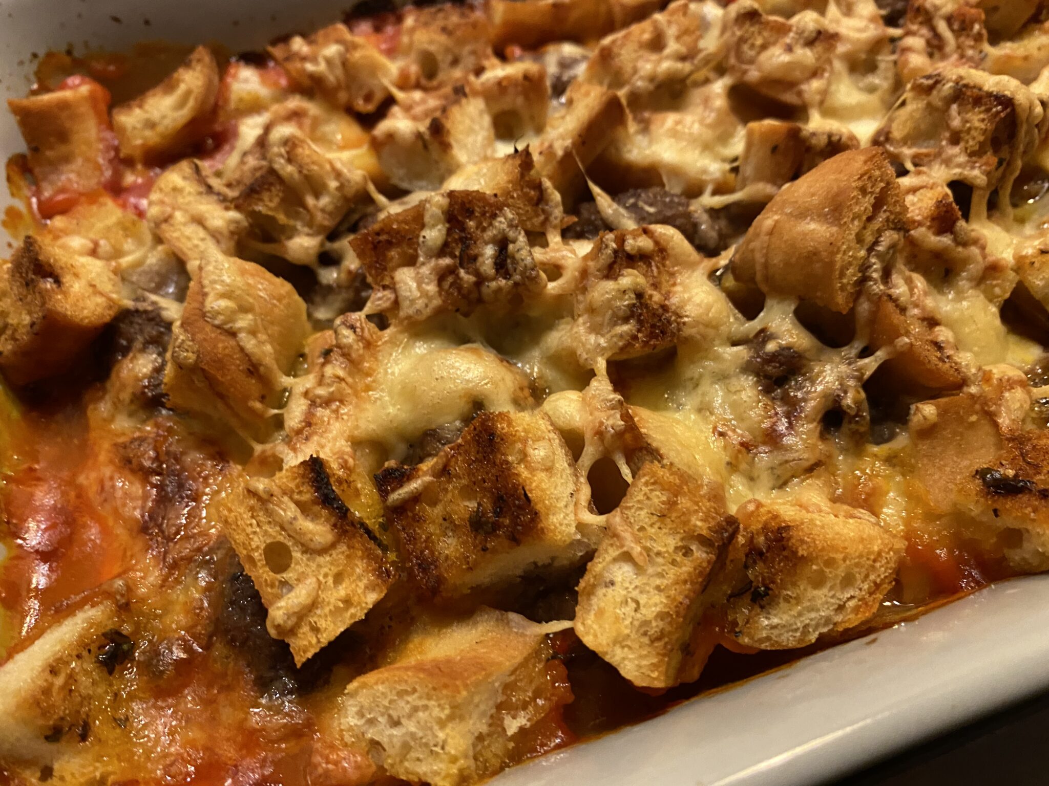 A close up of meatballs, chunks of crispy garlic bread topped with cheese in an oven tray.