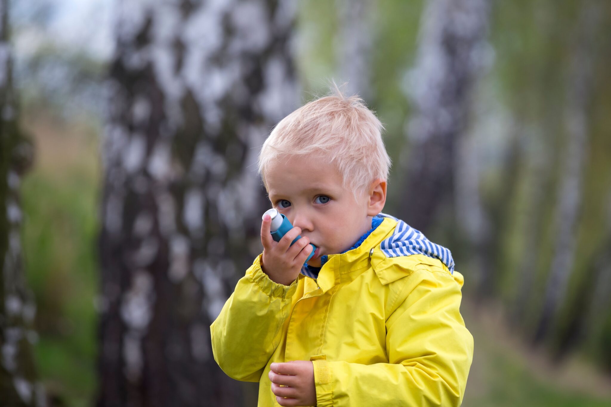 A little boy using an asthma inhaler outside in the colder weather.
