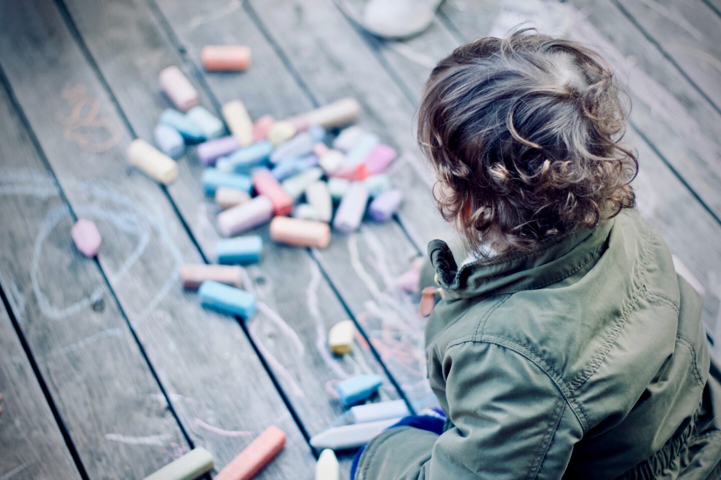 A boy playing with coloured chalks on the floor outside