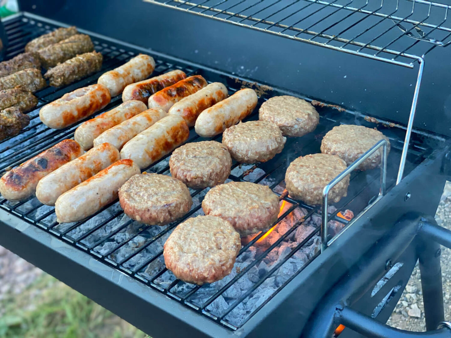 A bbq cooking burgers, sausage and lamb koftas.