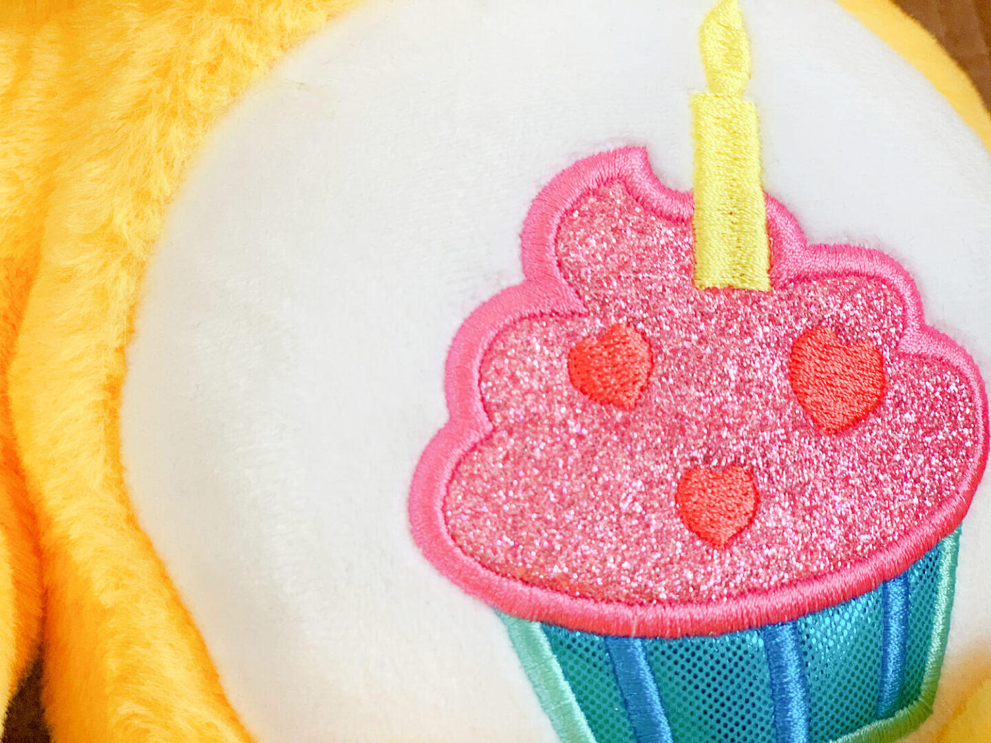 An embroidered pink and blue cupcake on a Care Bear teddy