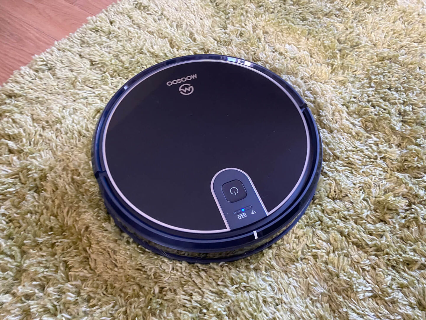 A robot vacuum cleaning a green long pile rug.