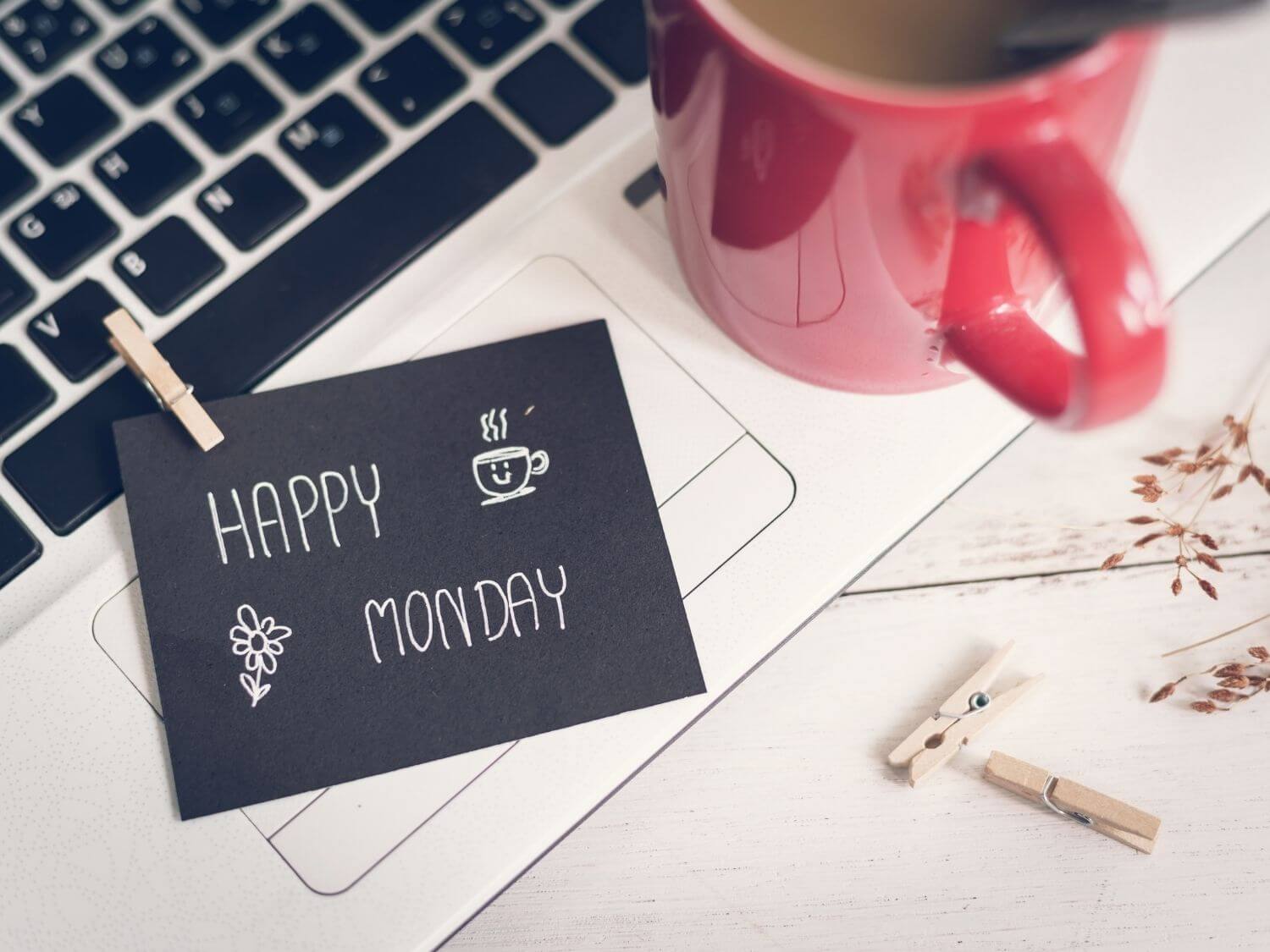 A laptop keyboard next to a red mug of tea and a little note saying "Happy Monday".