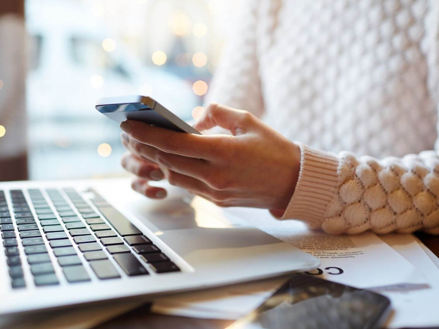 A lady sat at a desk with a laptop and her phone