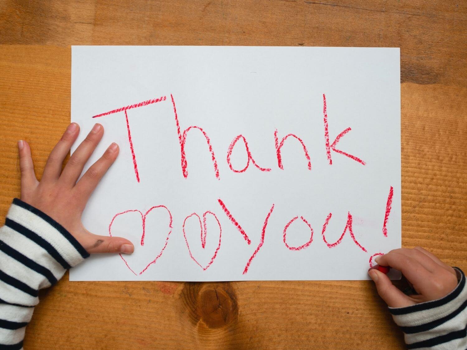 A child writing thank you on a piece of paper.