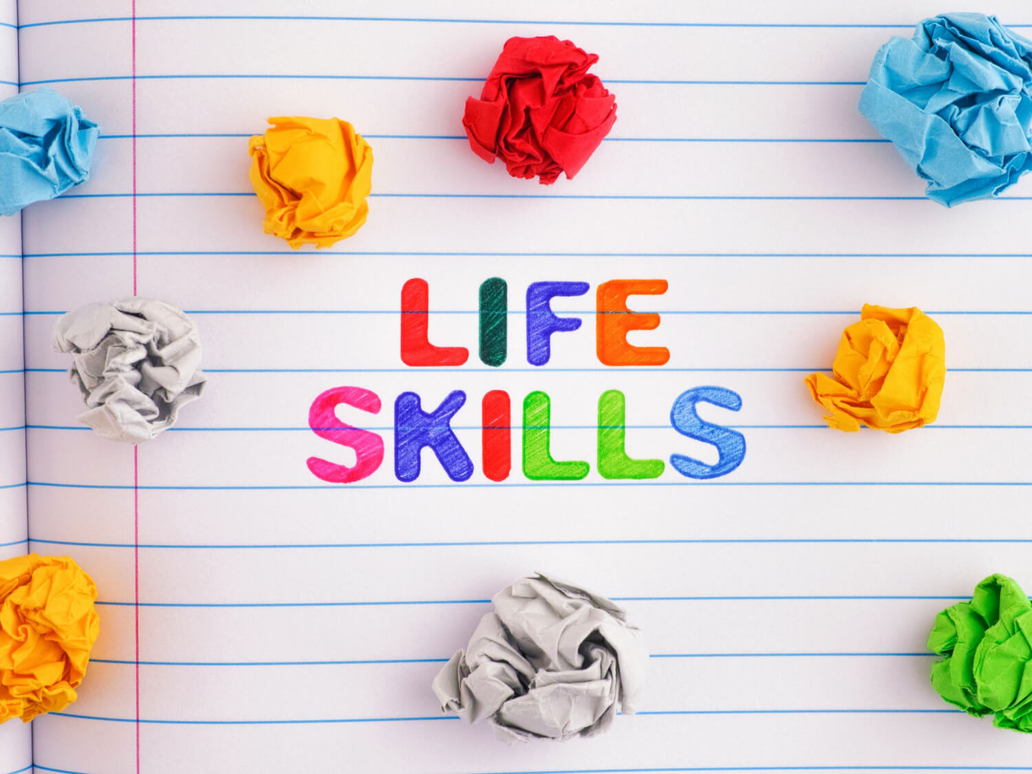 A lined piece of paper with the coloured in words "Life Skills". There are also scrunched up pieces of coloured paper surrounding it.