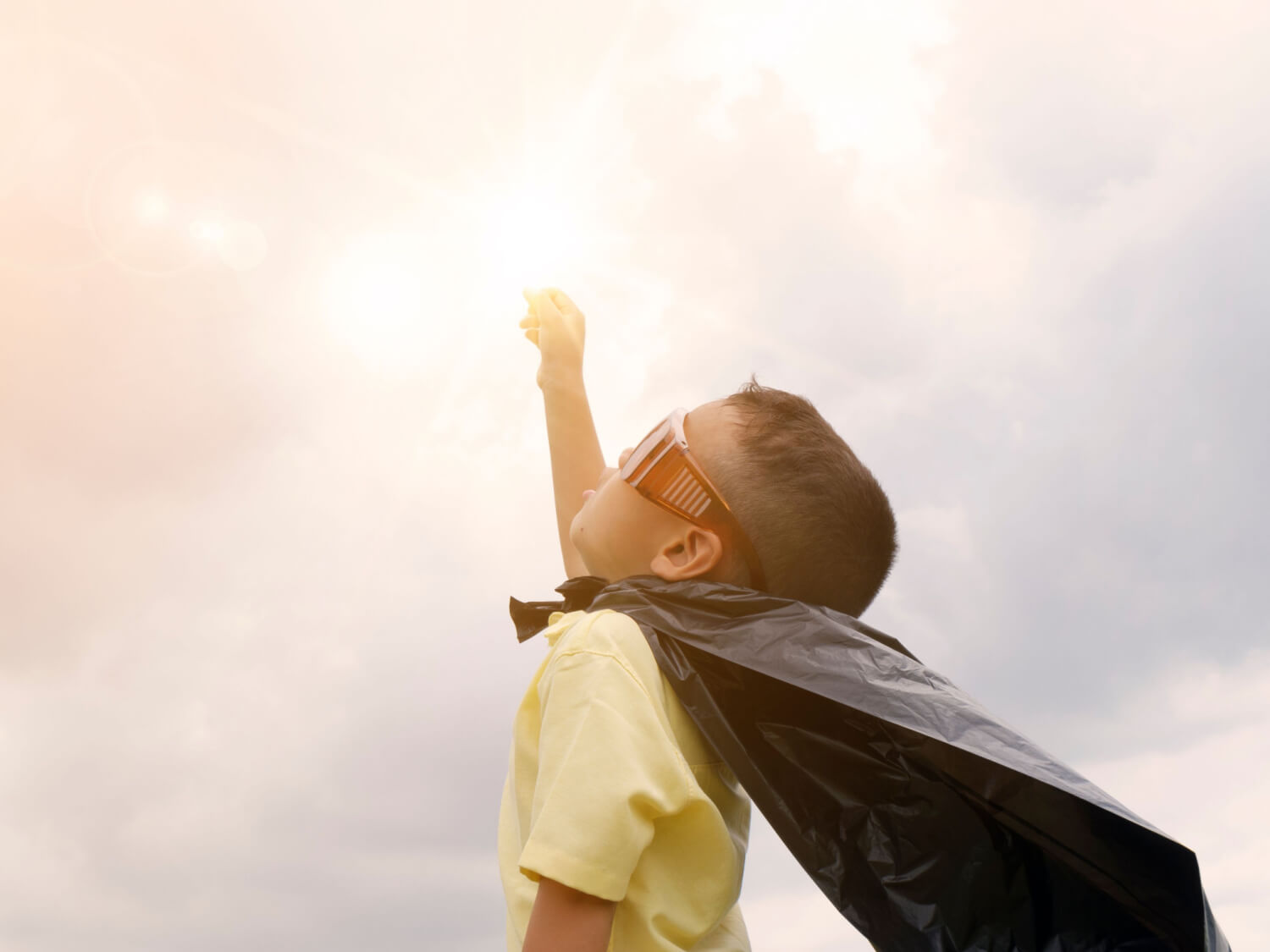 A little boy dressed up in a cape and goggles.
