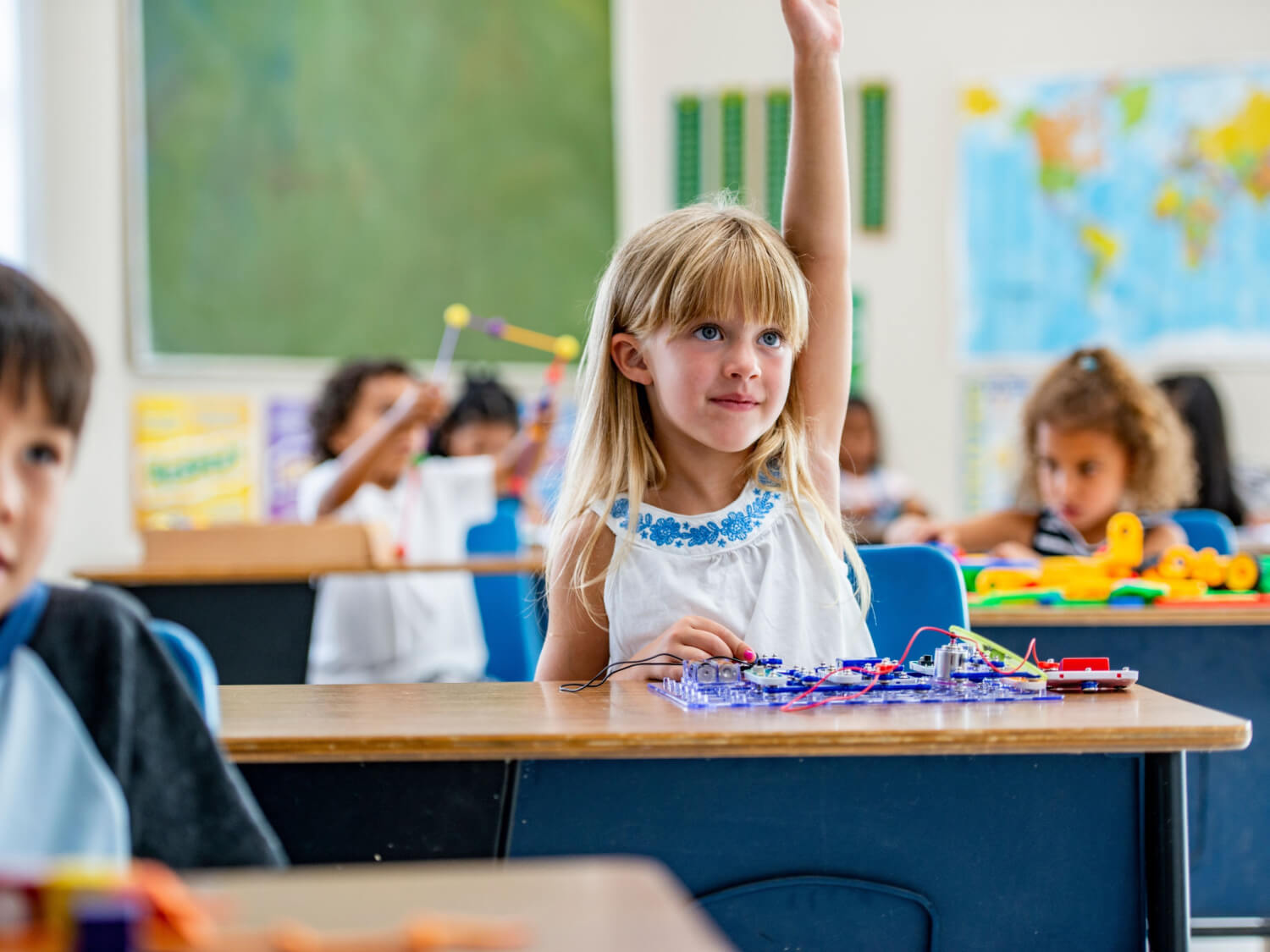 A young girl holding her hand up to ask a question in her school class.