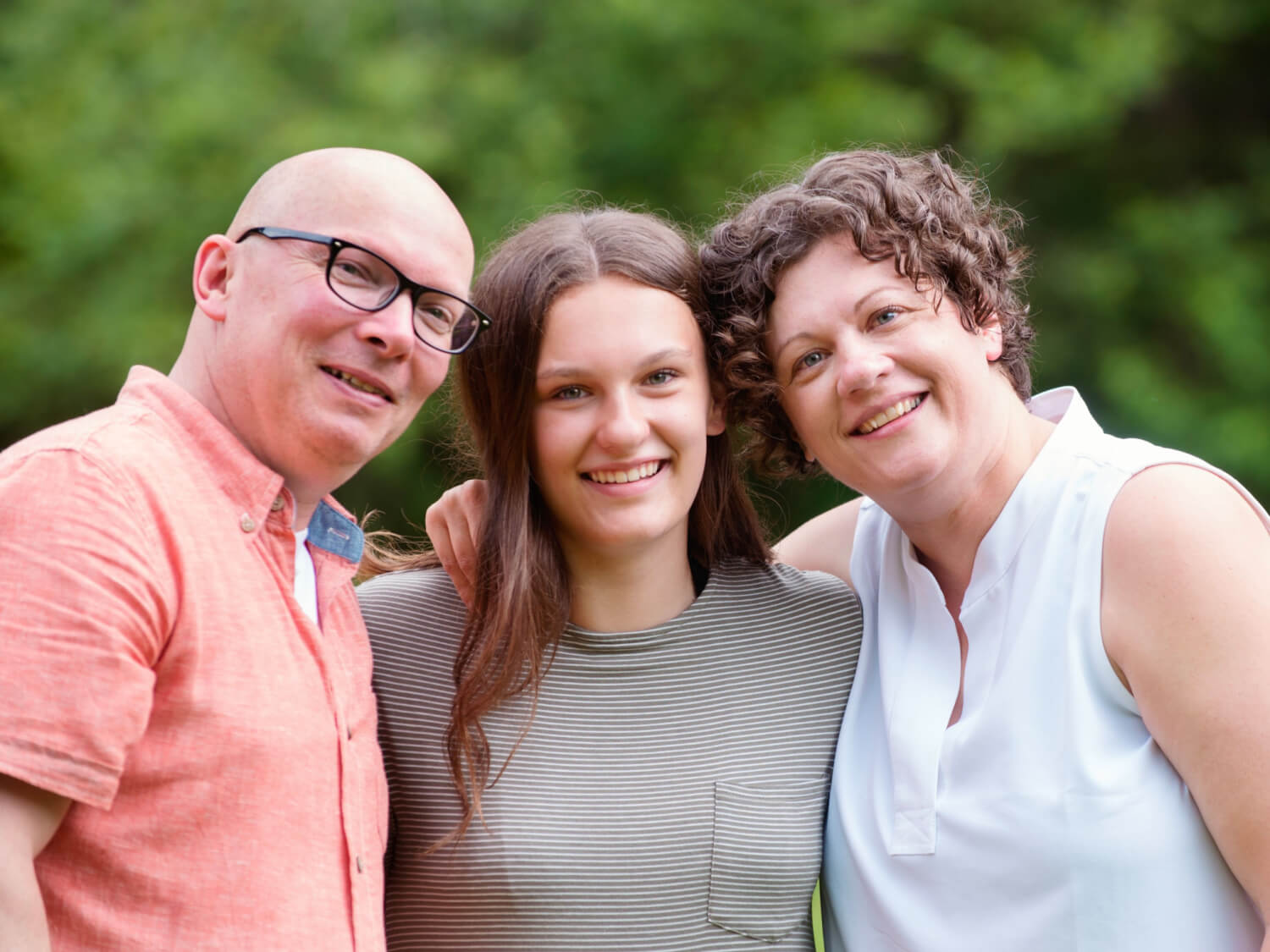 A family of three, mum, dad and daughter standing next to each other.