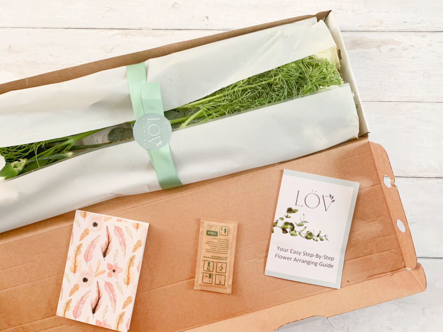 Flower stems in a cardboard box. Wrapped with a green compostable ribbon.