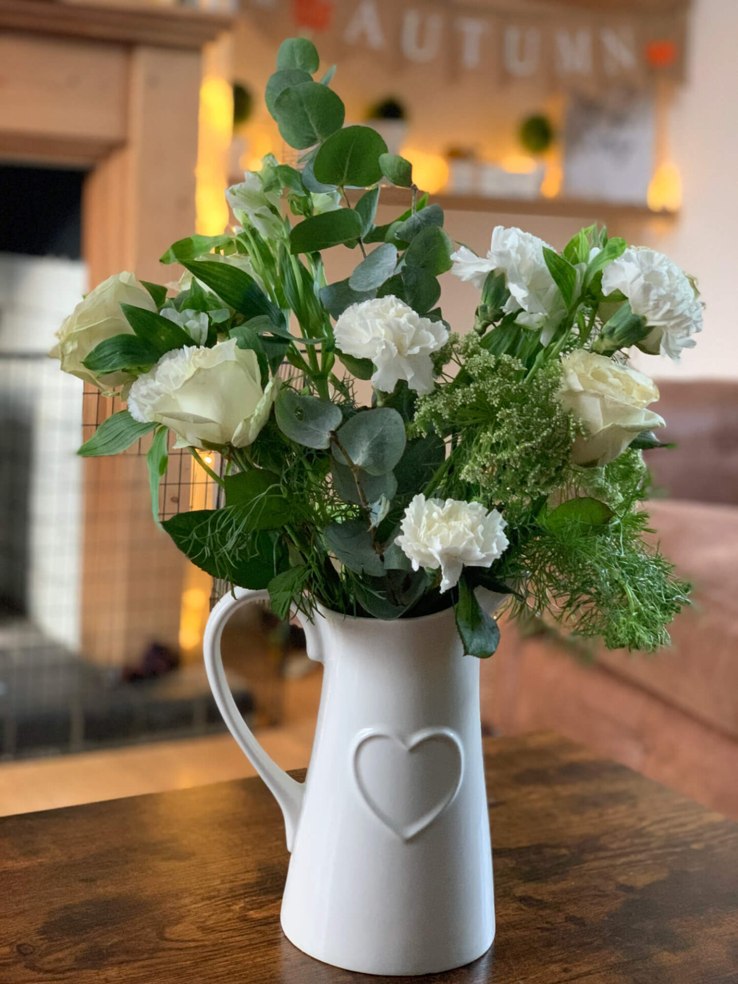 White carnations and roses with greenery in a white heart embossed jug.