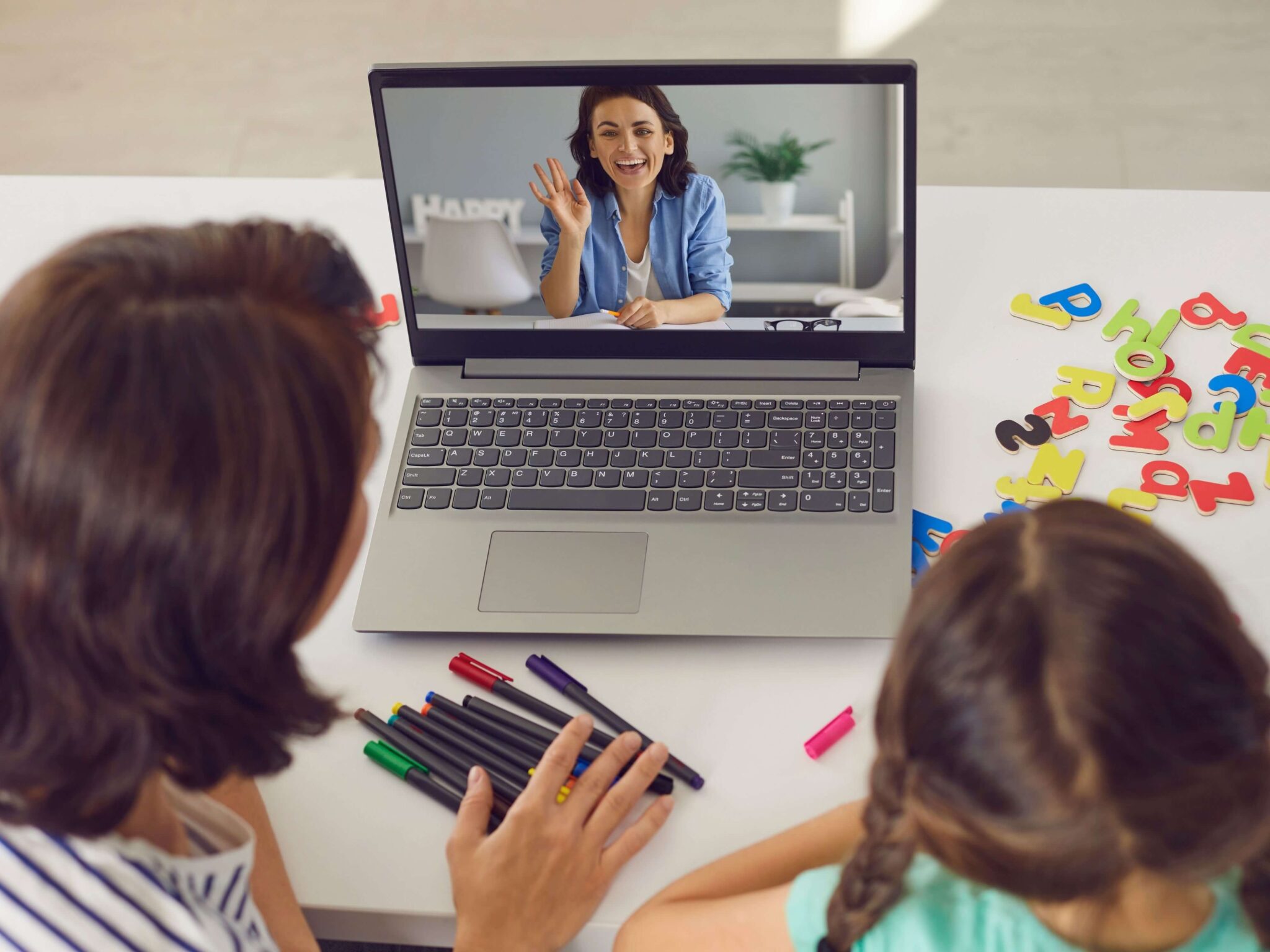 A mum and her daughter sitting in front of their laptop speaking to a tutor online.