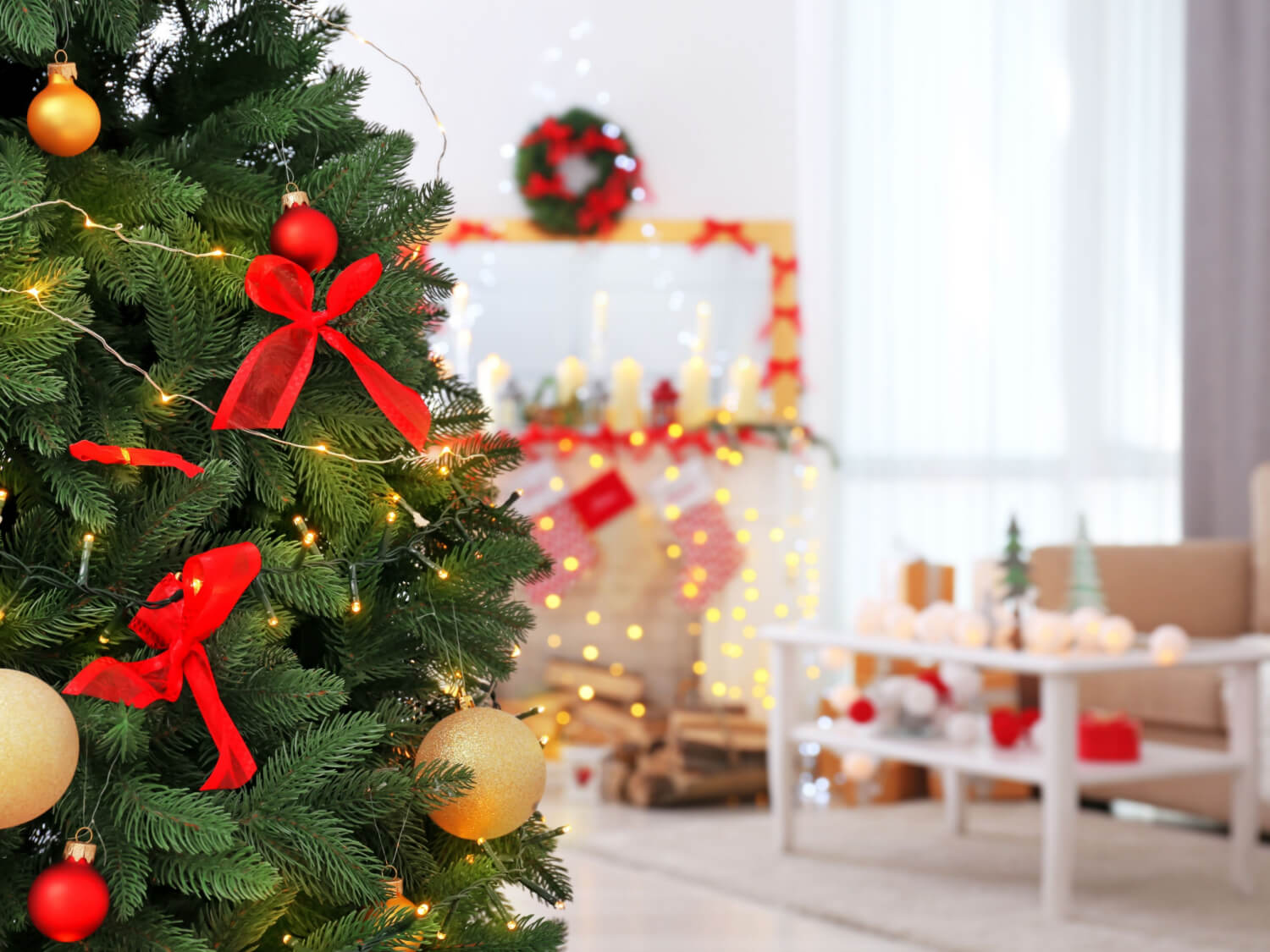 A living room decorated for Christmas with a green and red themed Christmas tree and twinkly lights and a wreath on the wall.