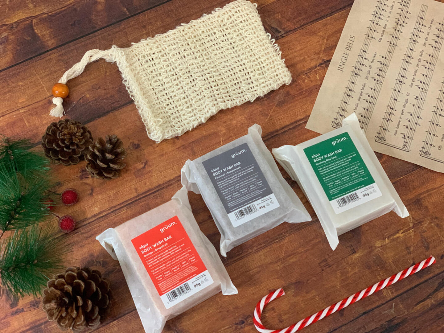 Soap bars and a crocheted soap bag next to Jingle bells sheet music, spruce sprigs and pinecones.