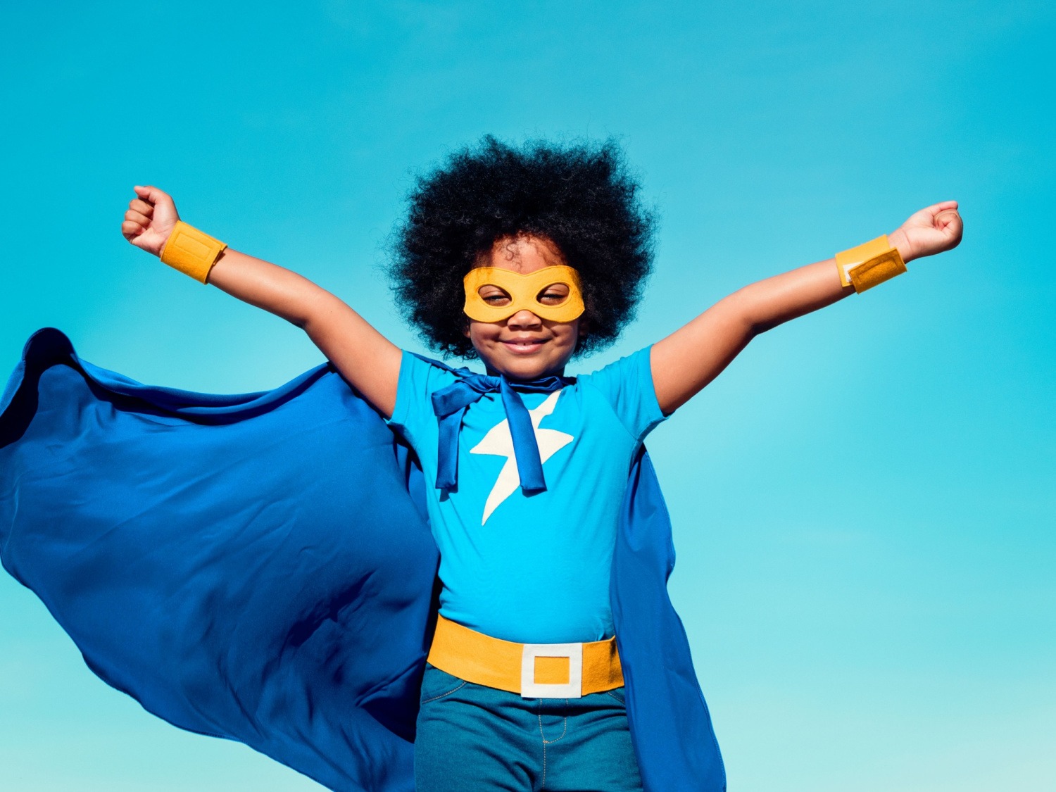 A girl wearing a blue superhero cape and goggles.