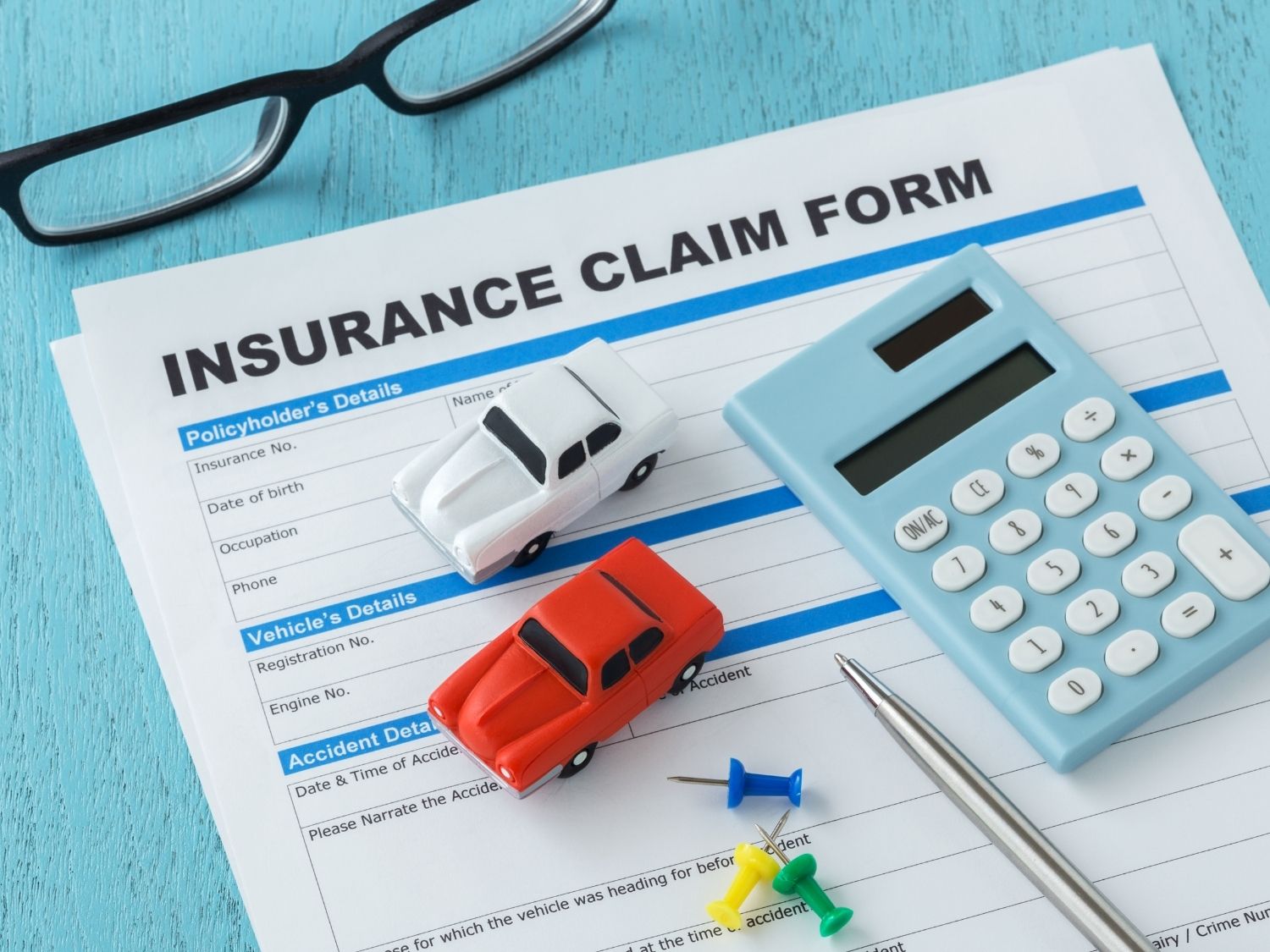 An car insurance claim form with toy cars on top and a calculator and pen.