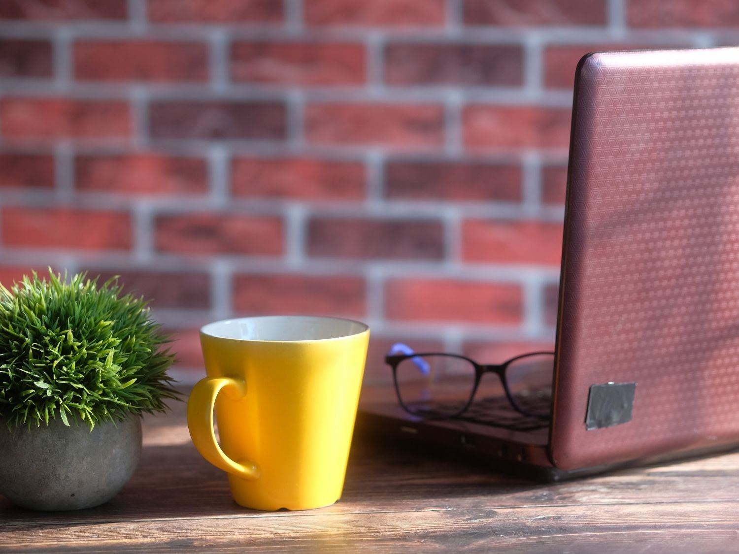 A yellow mug of tea and an artificial plant next to an open laptop.
