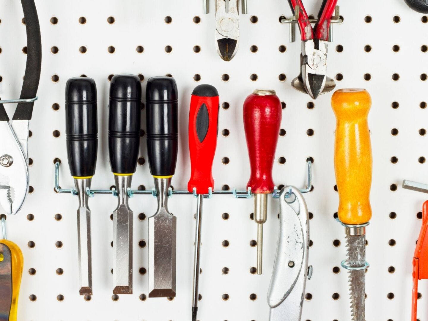 A white pegboard holding tools including screwdrivers, a blade and plyers.