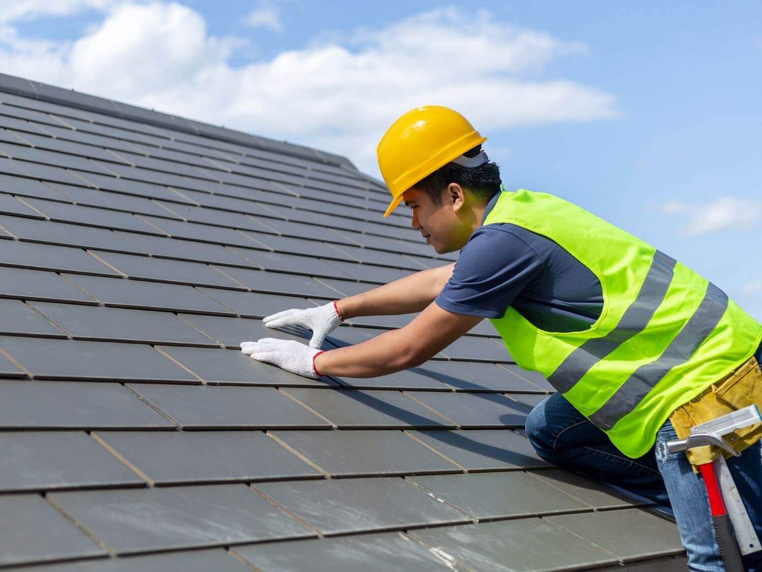 A worker laying tiles on the roof of a house.