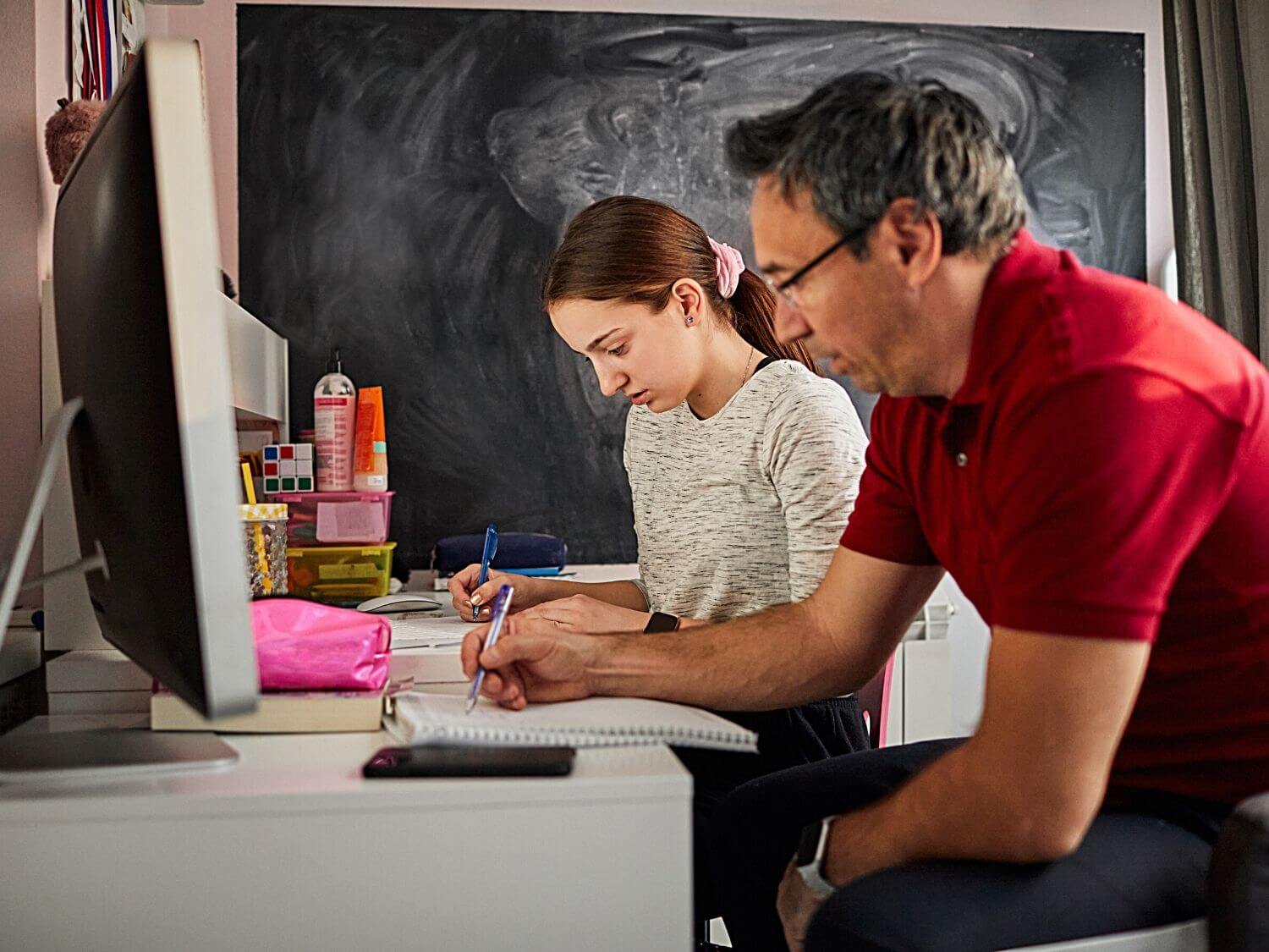 A father and daughter sitting at a desk writing.