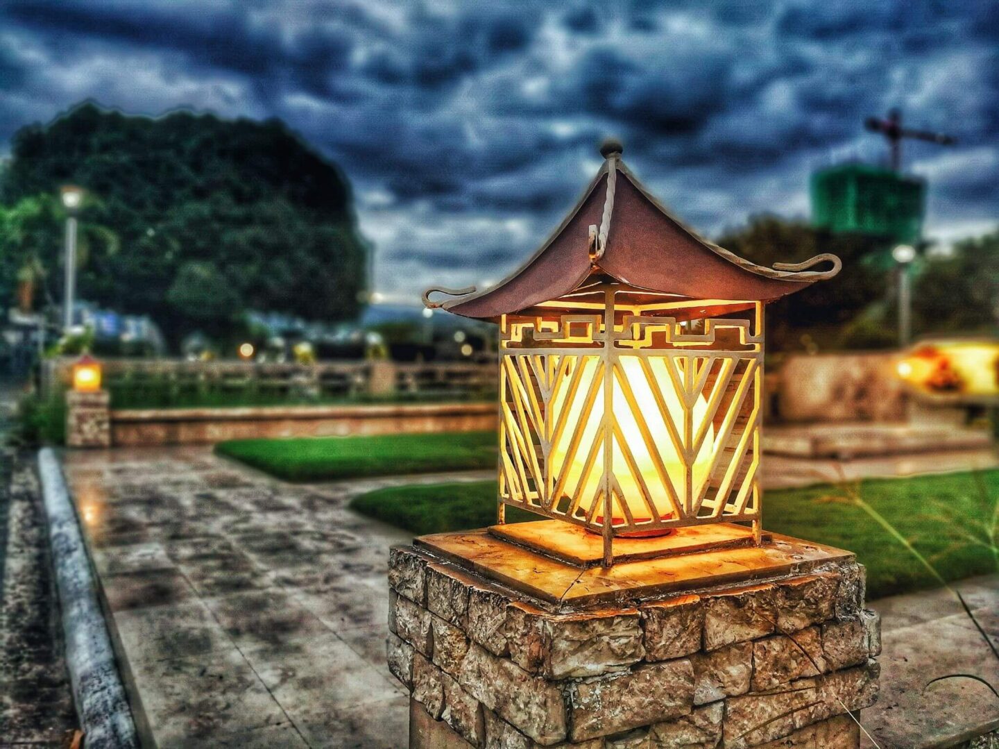 A brick pillar in a garden with a lantern light on top.