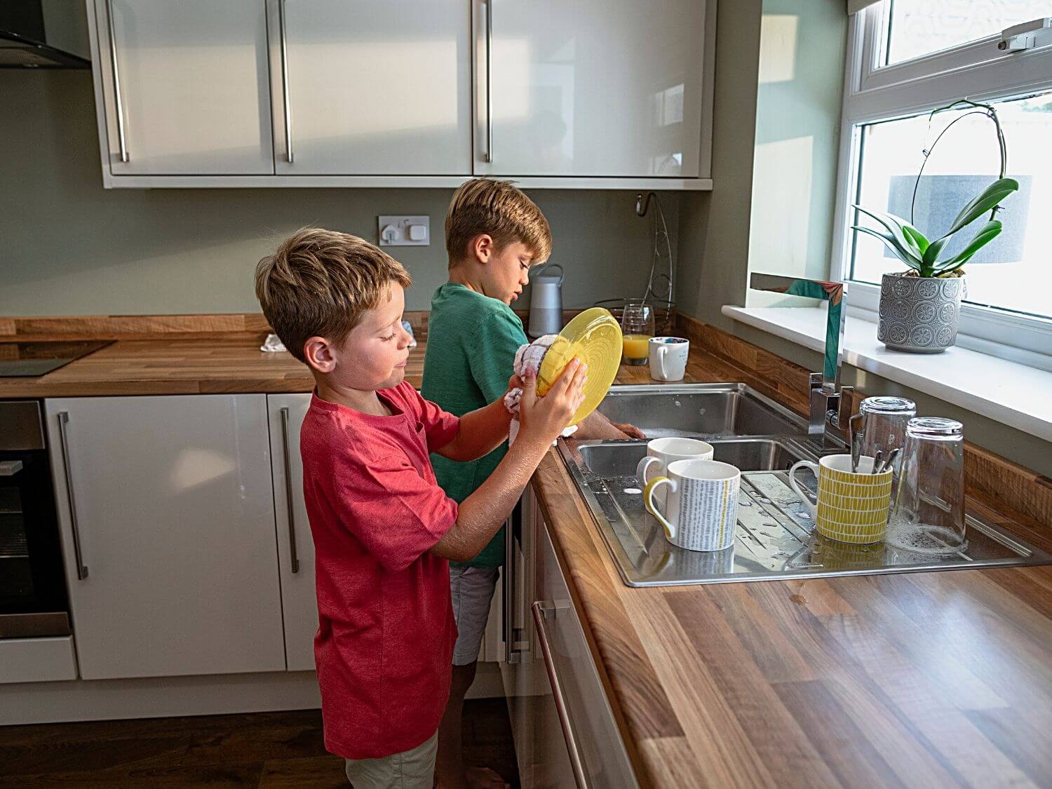 Two young boys washing up dishes and cups at the sink.