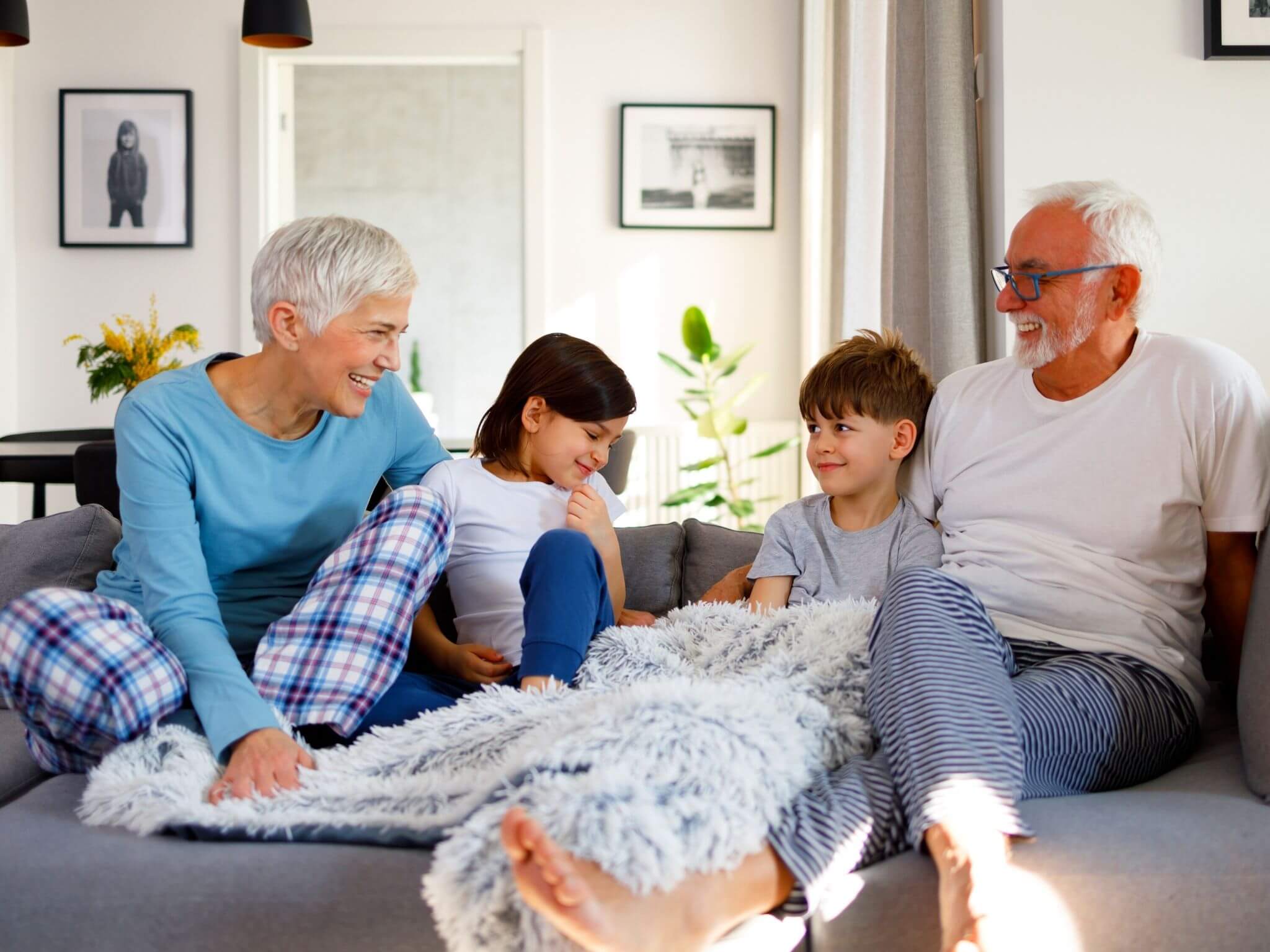 Grandparents sitting with their young grandaughter and grandson on the sofa. They are all wearing their pyjamas.