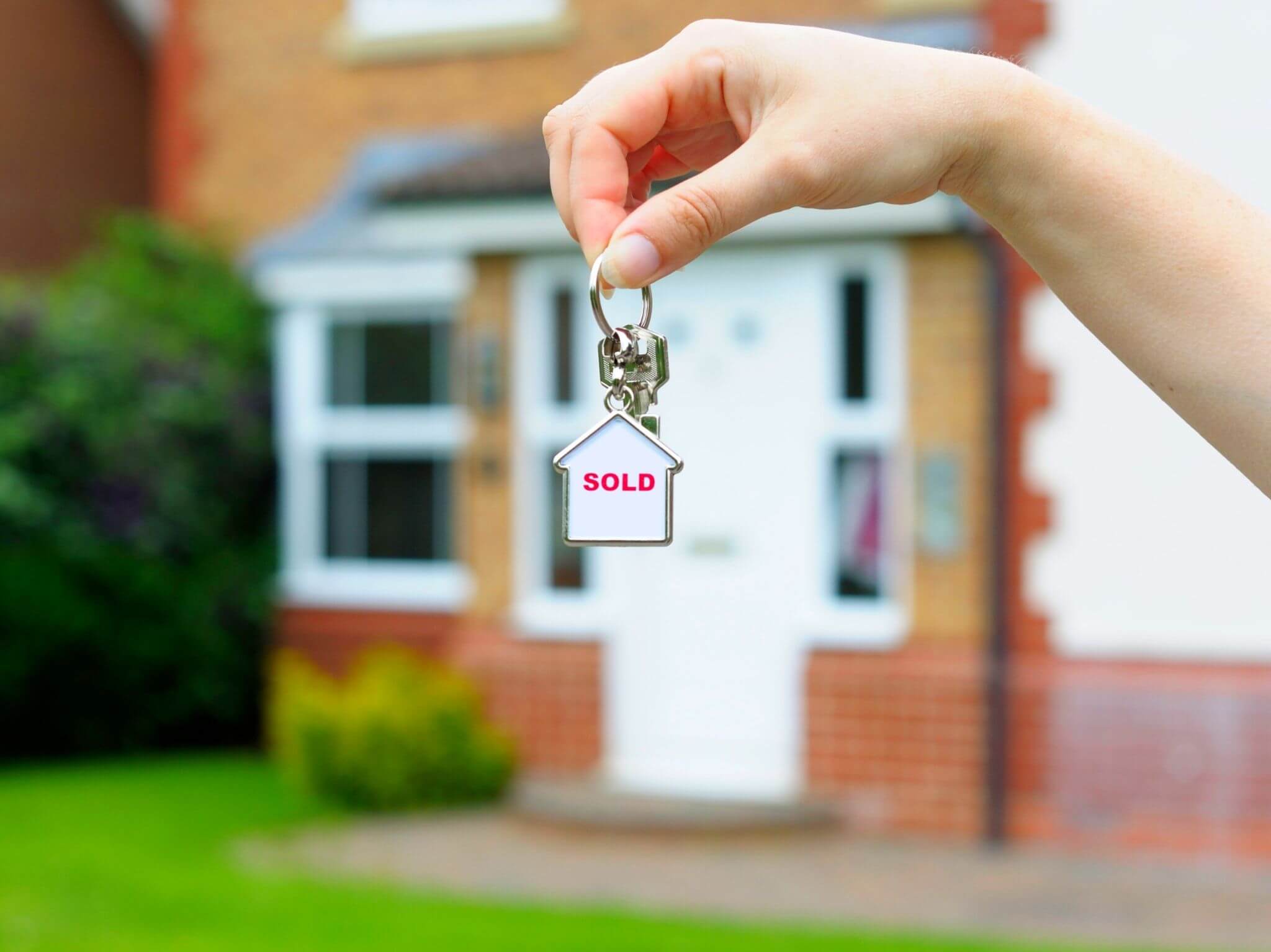 A close up of a lady's hand holding a key to their new home which is blurred out in the background.