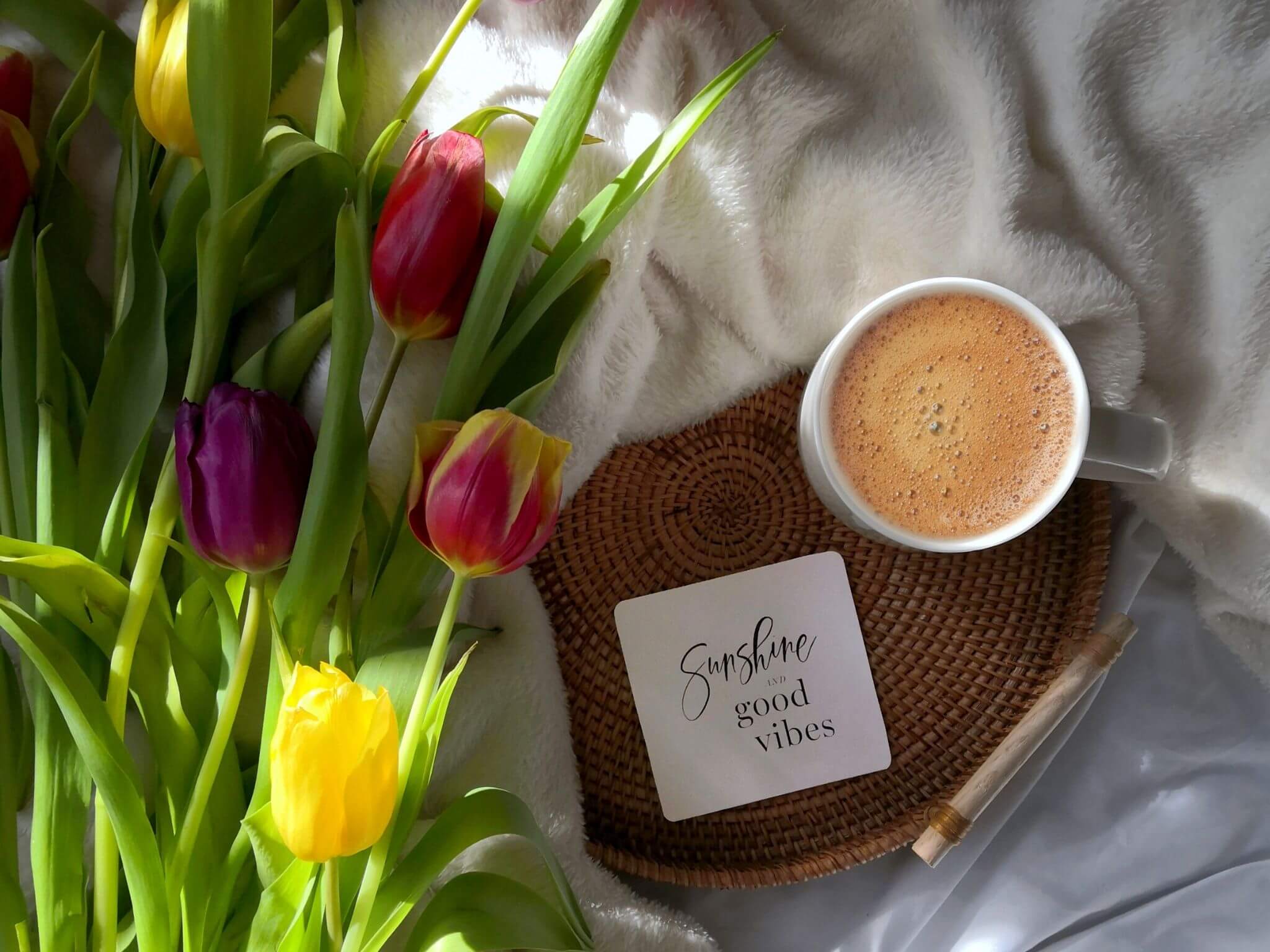 A bunch of tulips on a worktop with a cup of coffee and a affirmation card saying 'Sunshine and good vibes'.