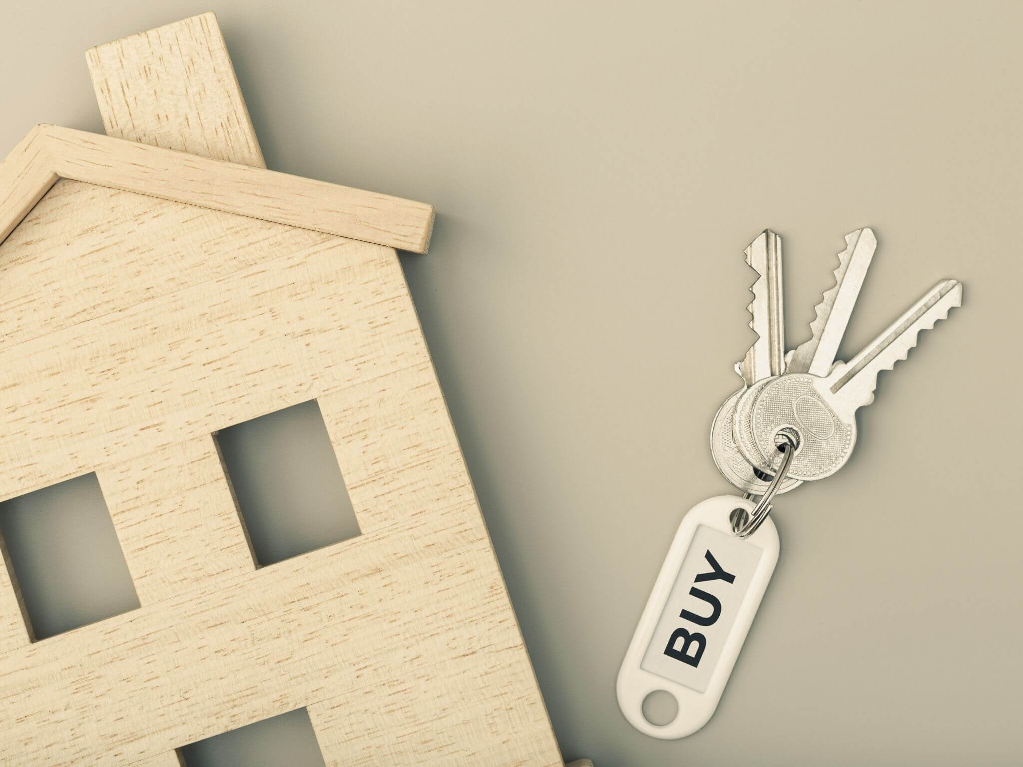 A wooden laser cut model house with a set of keys next to it with a keyring reading 'buy'.