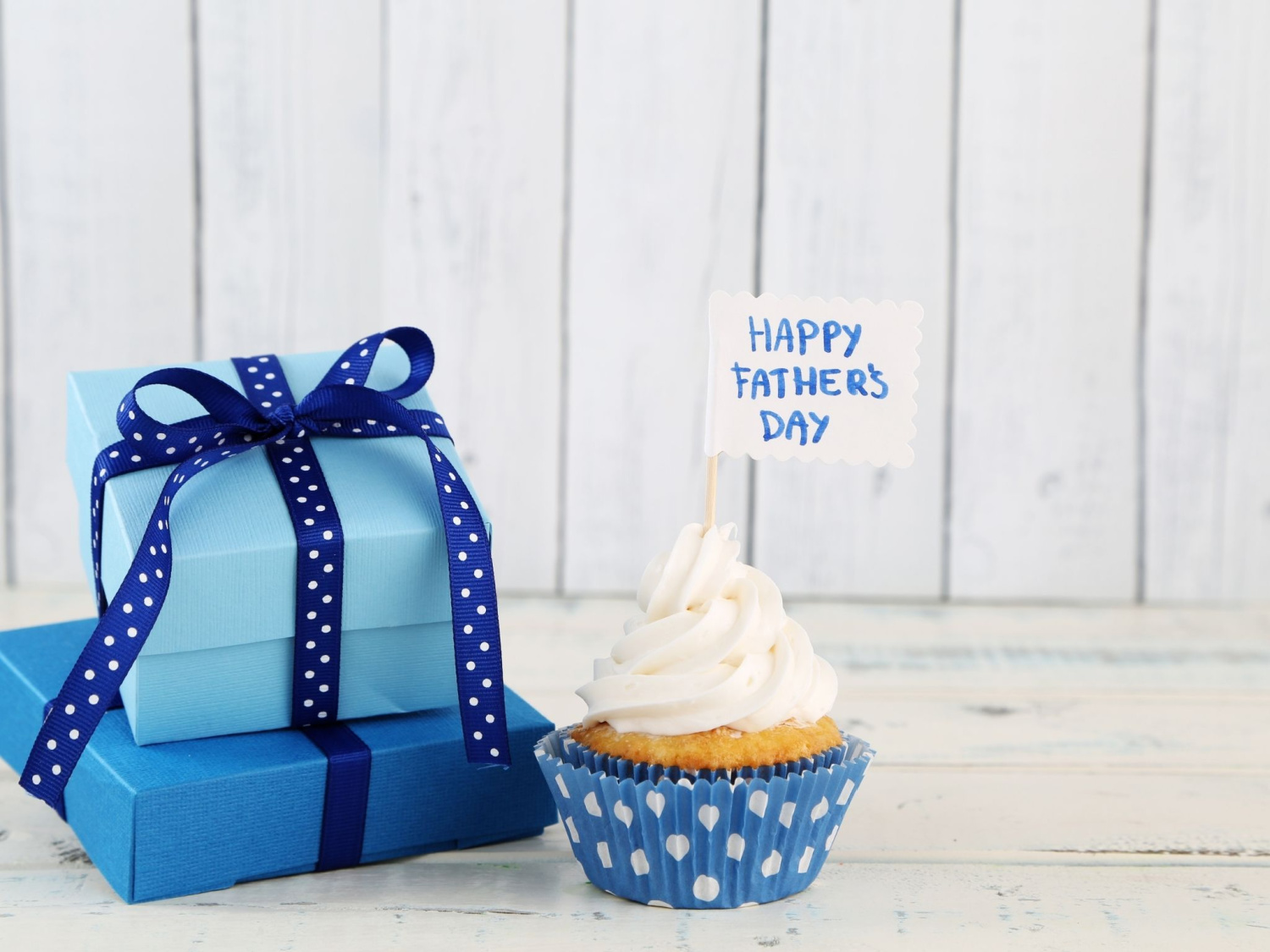 Two blue presnts stacked next to a cream cupcake.