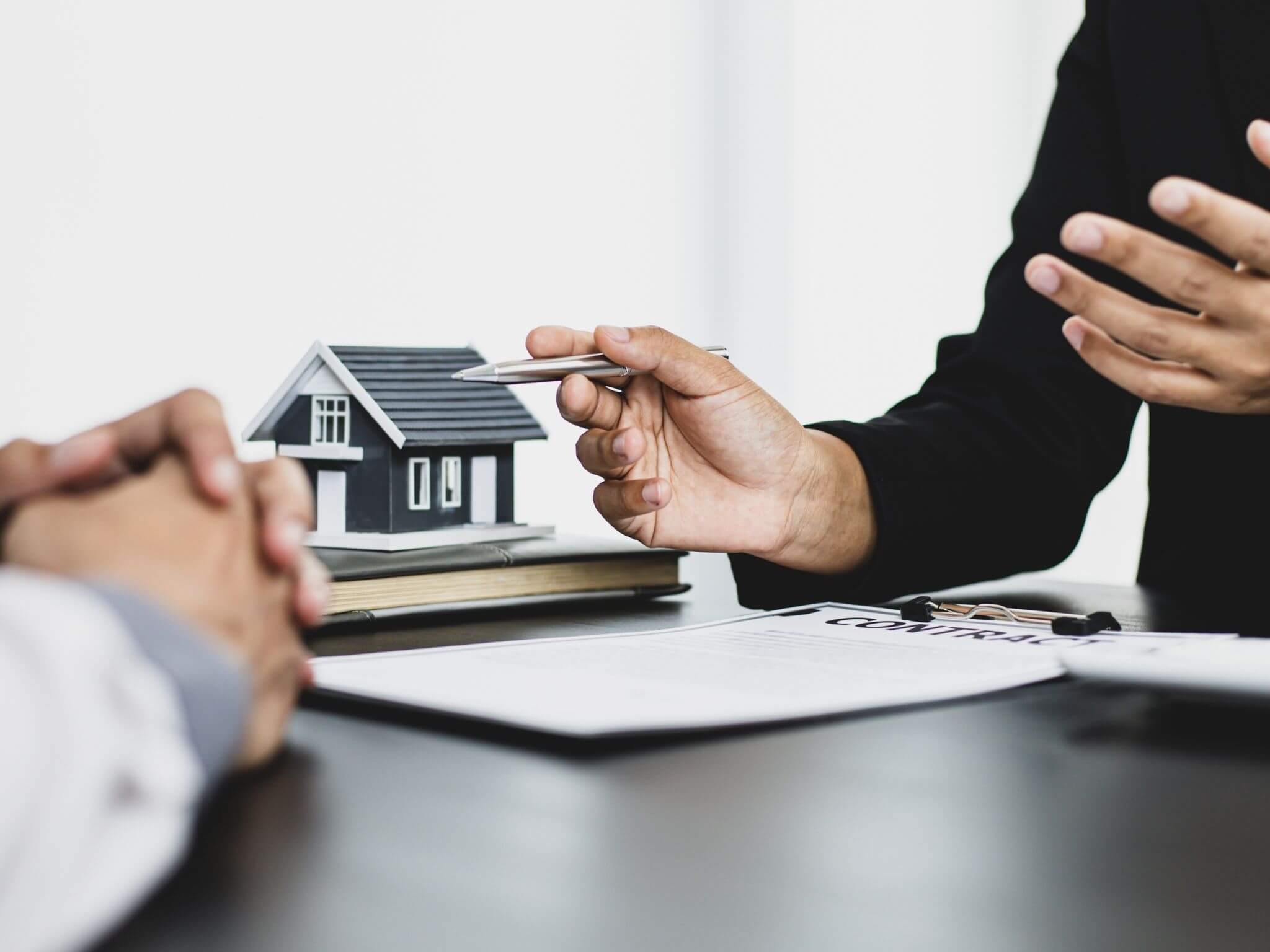A customer sat at a desk with a real estate agent and a miniature model house in between them on the desk.