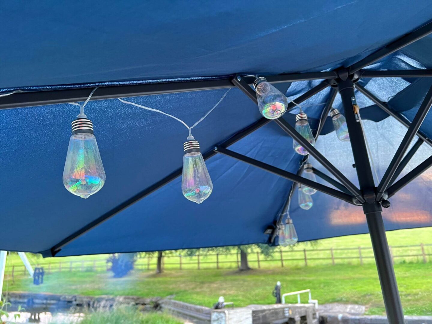 A navy blue umbrella on a glass patio table with iridescent solar light bulbs hanging inside.